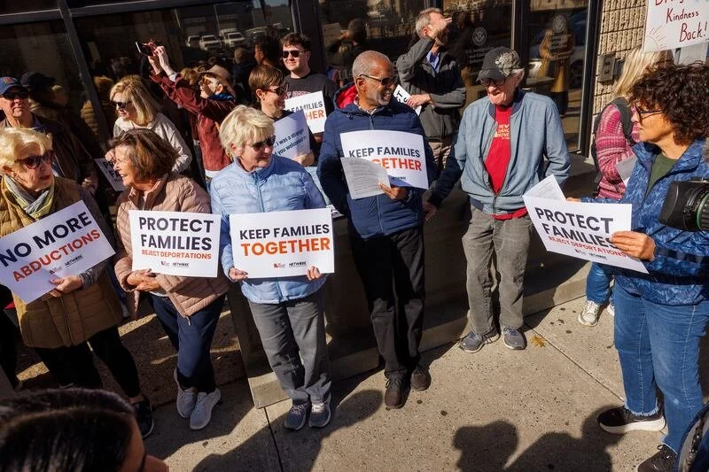 Group of people protesting on sidewalk, holding signs that say 'Protect Families,' 'Keep Families Together,' and 'No More Abductions'.