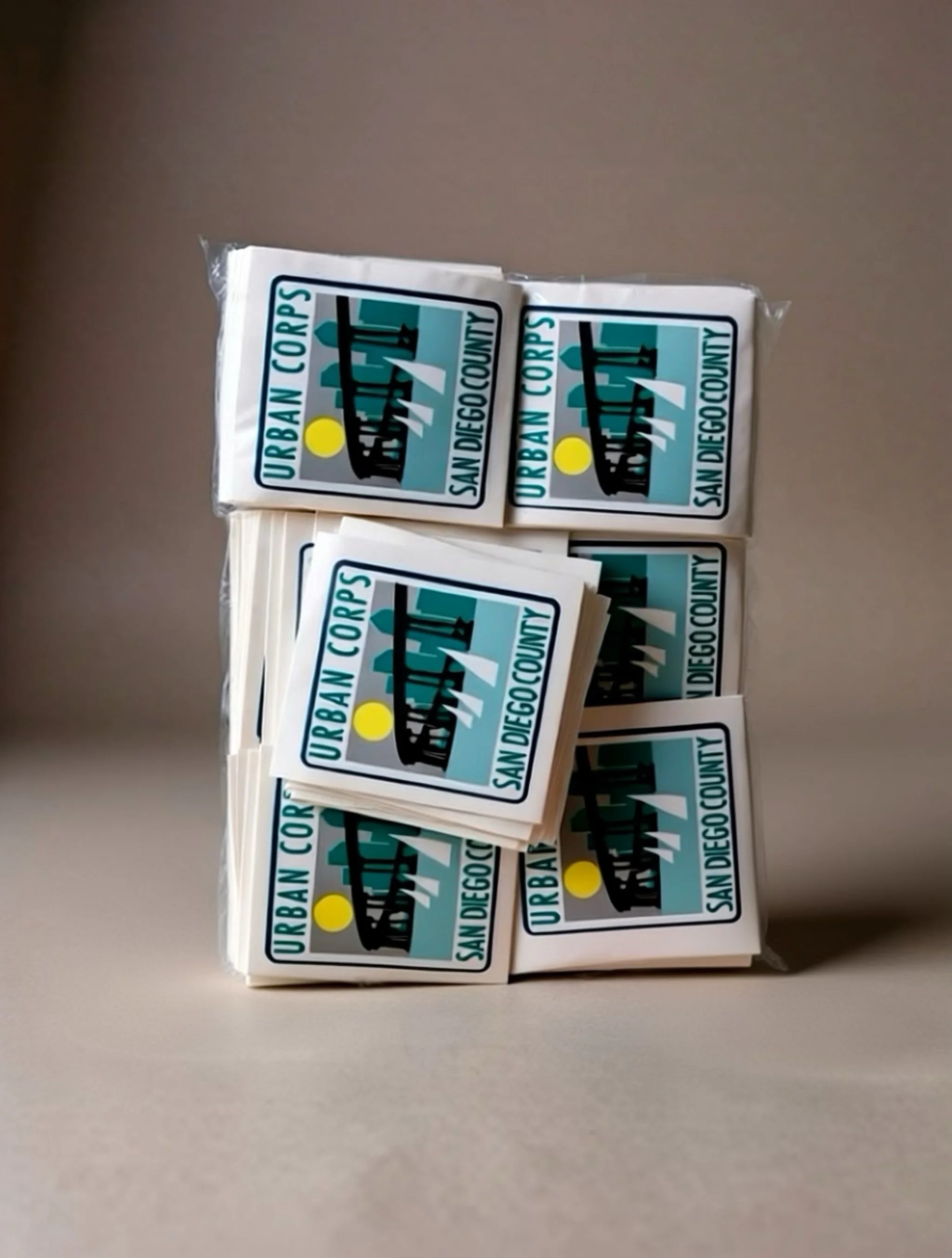 Stack of stickers with city skyline, sun, and the text 'Urban Corps, San Diego County'.