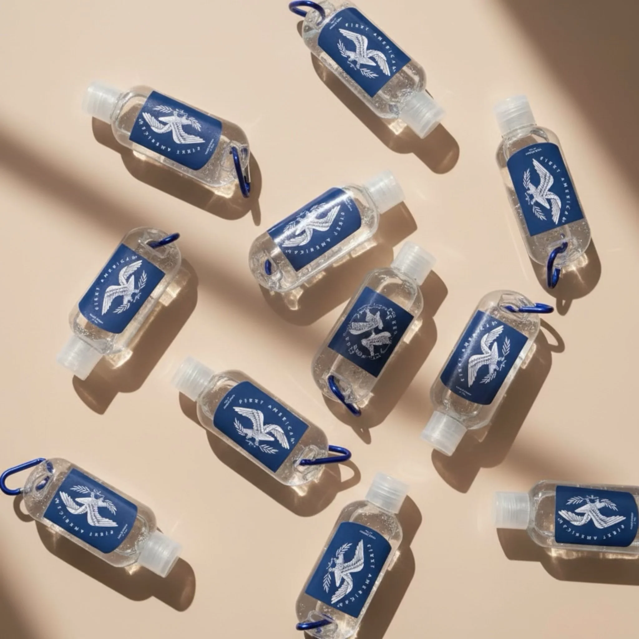 Multiple small bottles of hand sanitizer with blue labels featuring an eagle emblem, arranged on a light-colored surface with shadows.