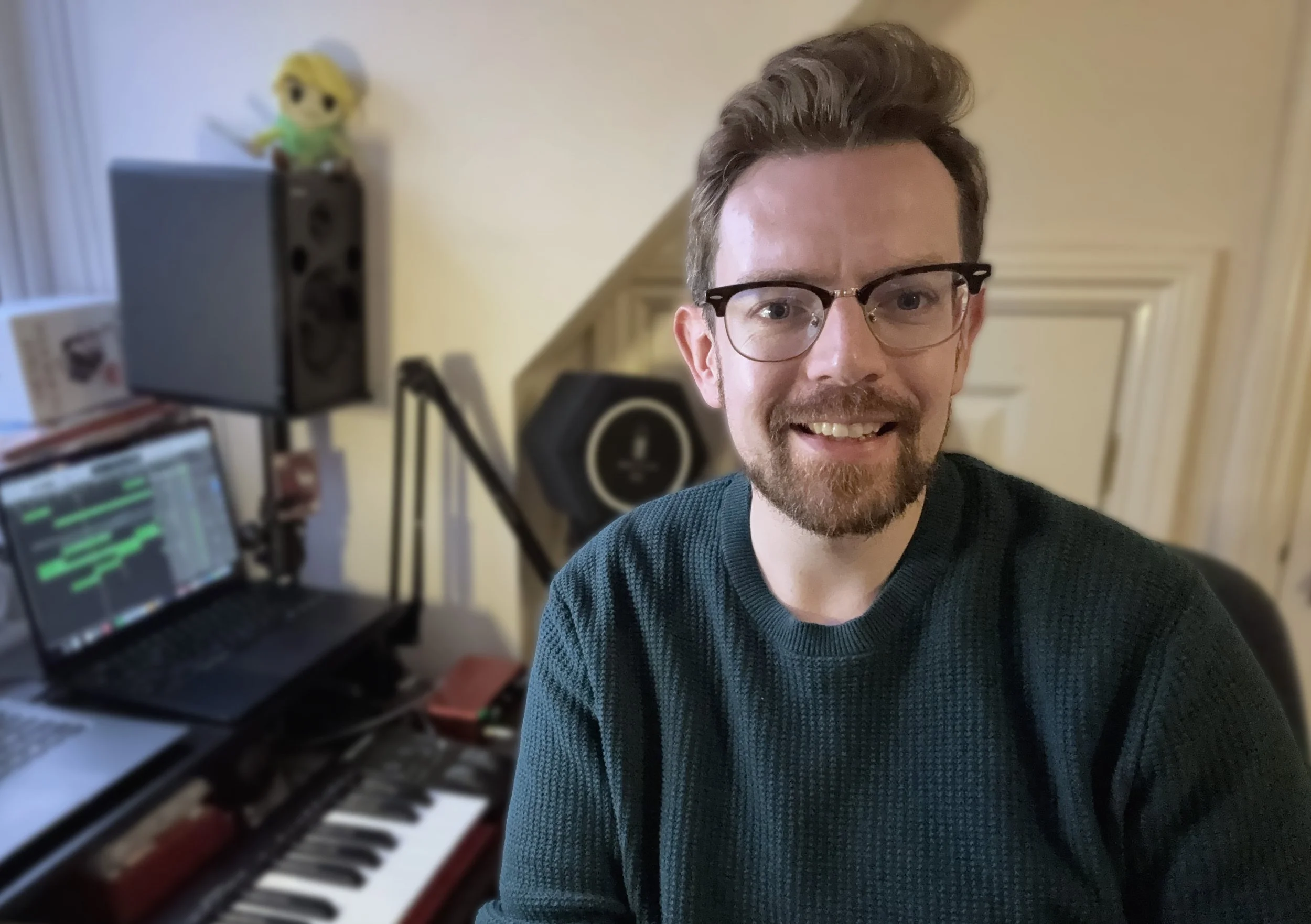 Paddy smiling in foreground, keyboard and laptop in bedroom studio in background