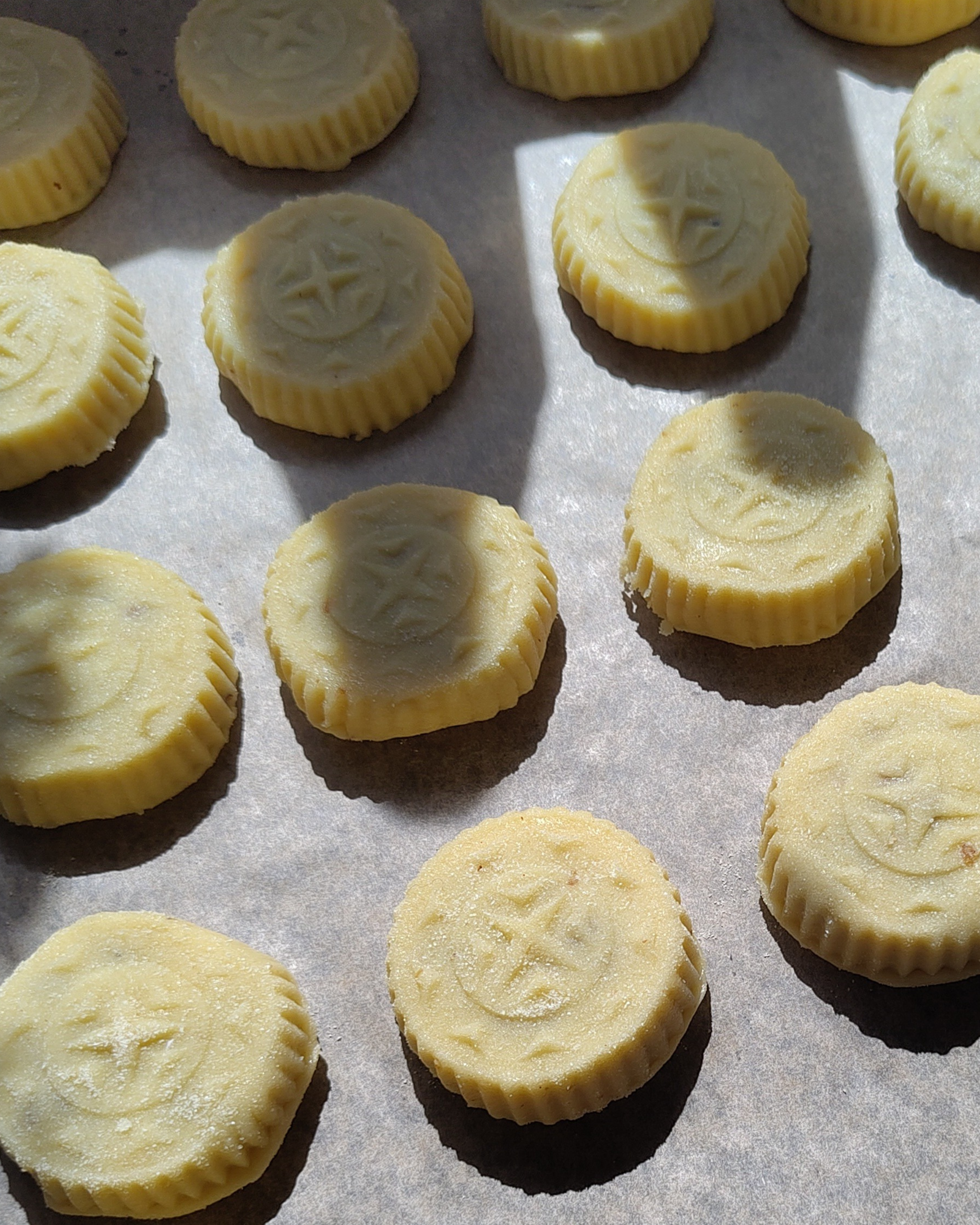 Close-up of unbaked cookies with a star and moon design on top, on a parchment-lined baking sheet.