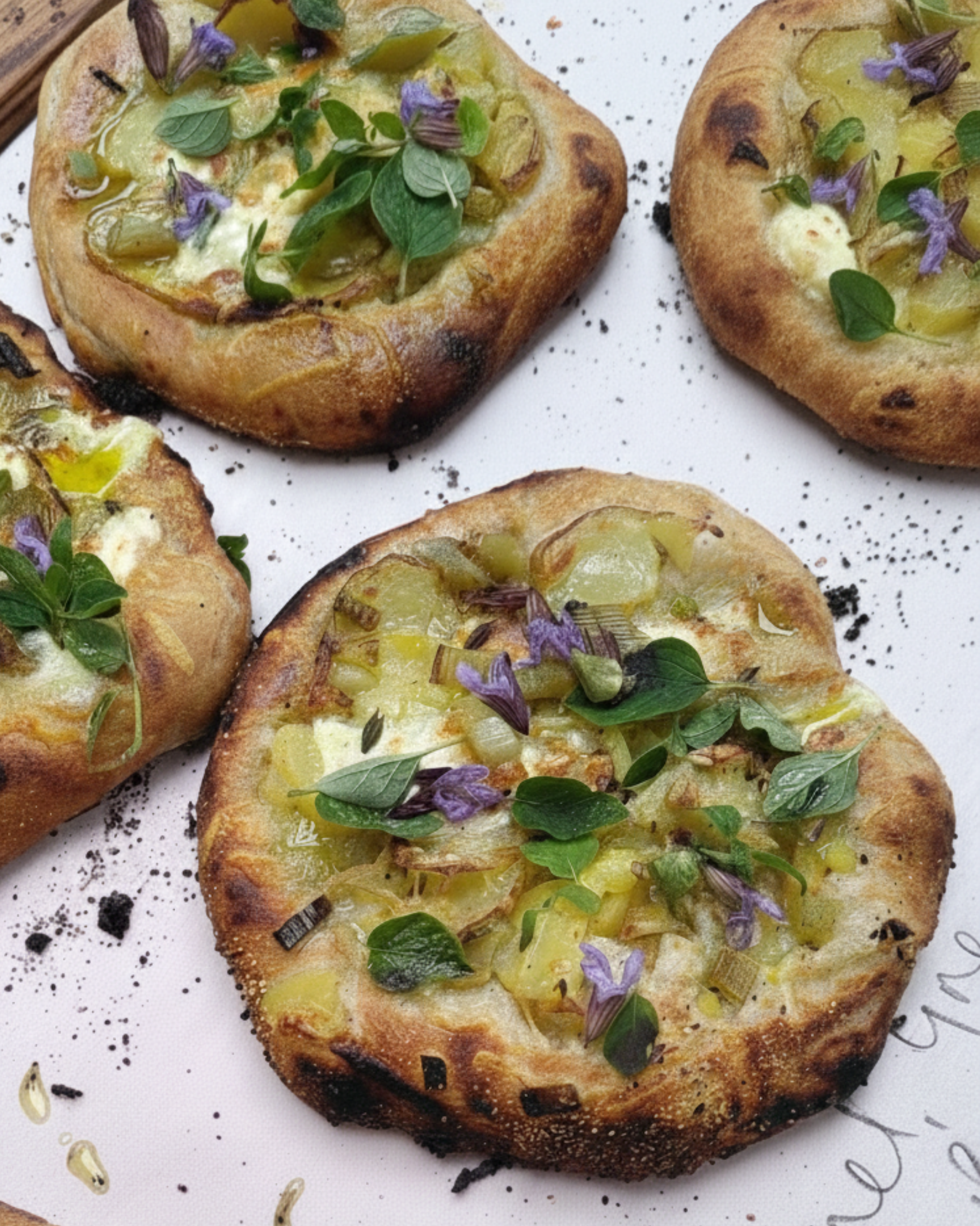 Close-up of toasted bread slices topped with cheese, chopped onions, and purple edible flowers, garnished with fresh herbs, on a white plate.