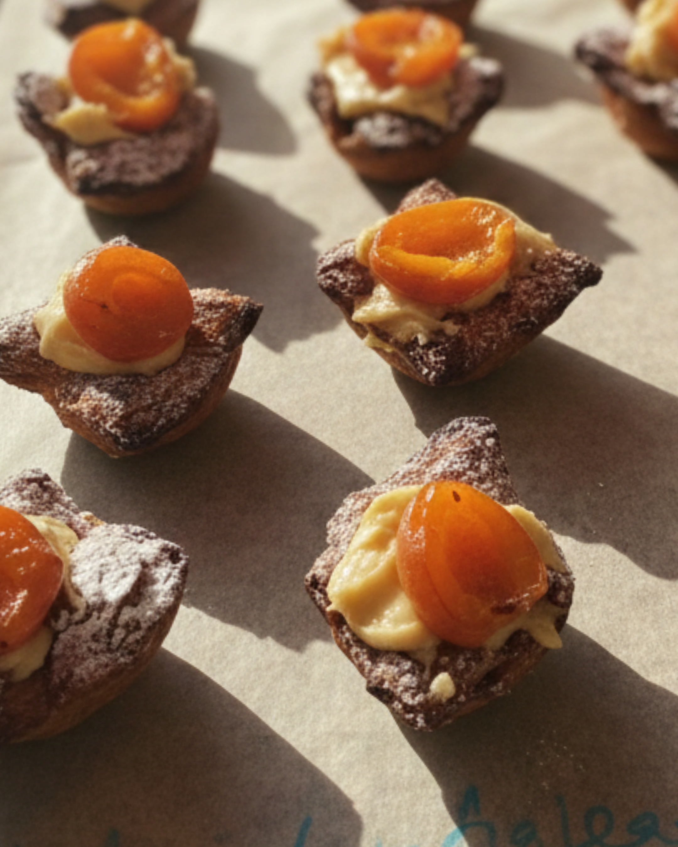 Miniature chocolate desserts topped with a dollop of cream and an apricot, arranged on parchment paper.