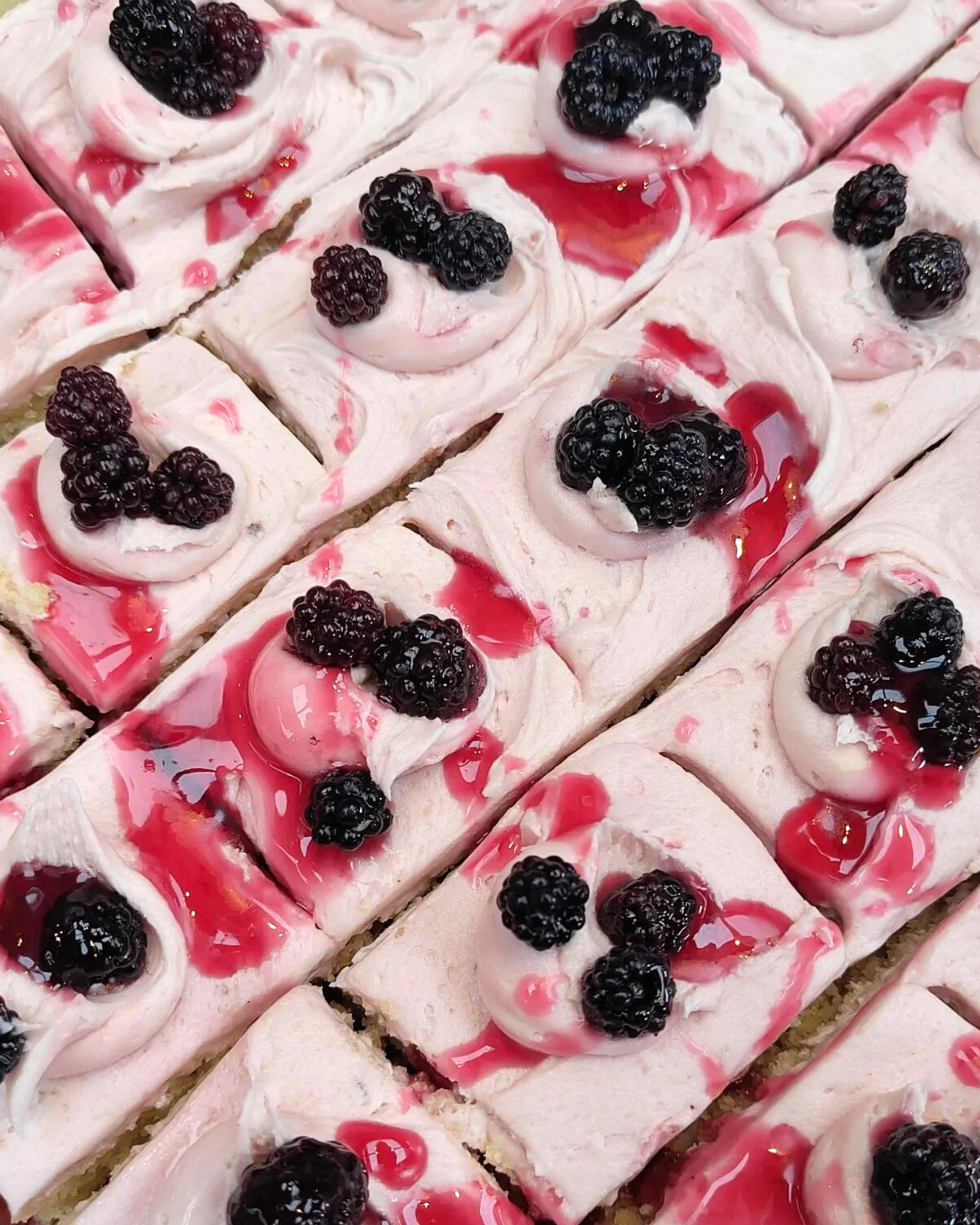 Sliced blackberry dessert topped with blackberries and drizzled with pink and red syrup.