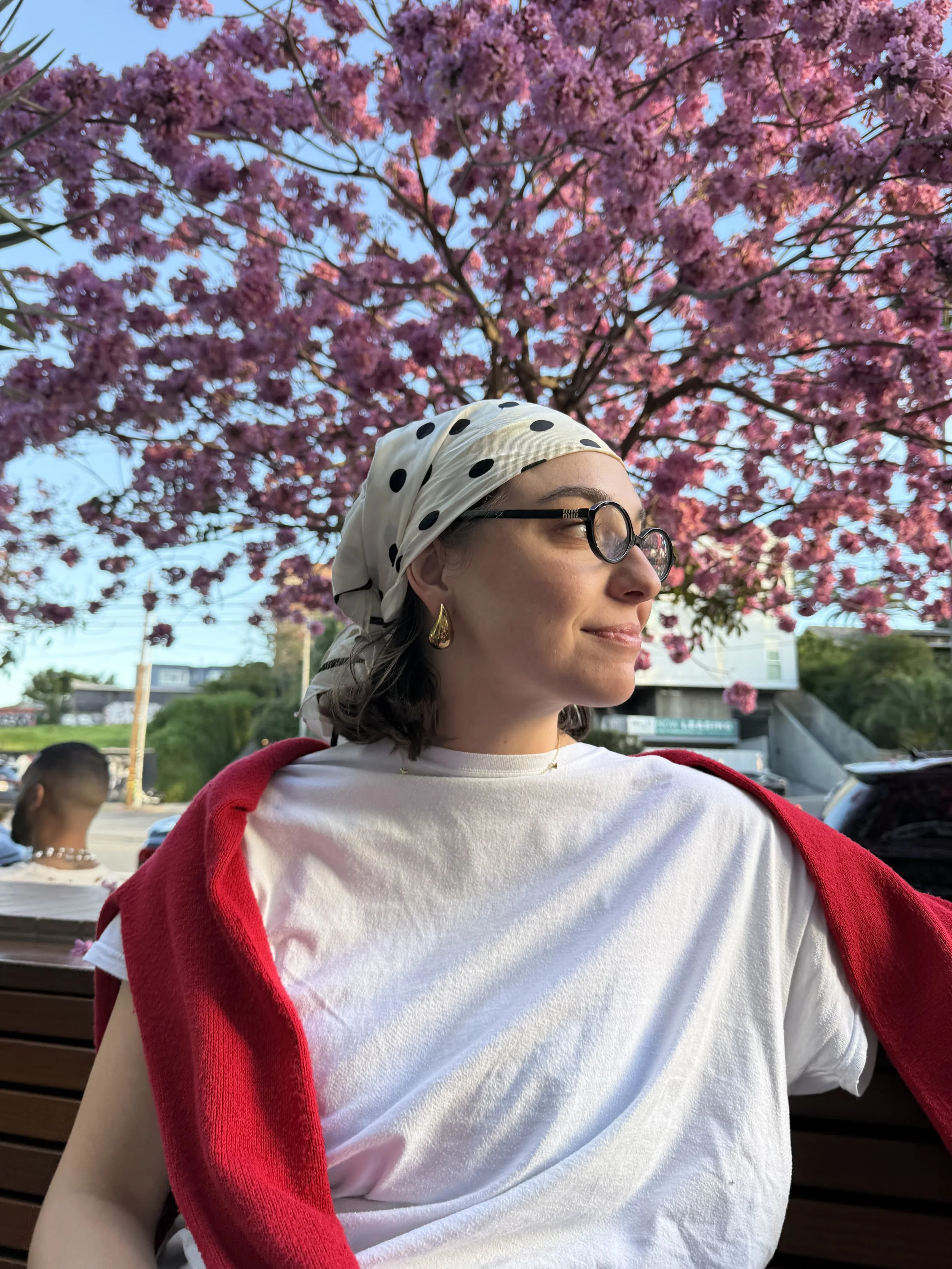 A woman sitting on a park bench with pink cherry blossom trees in full bloom behind her.