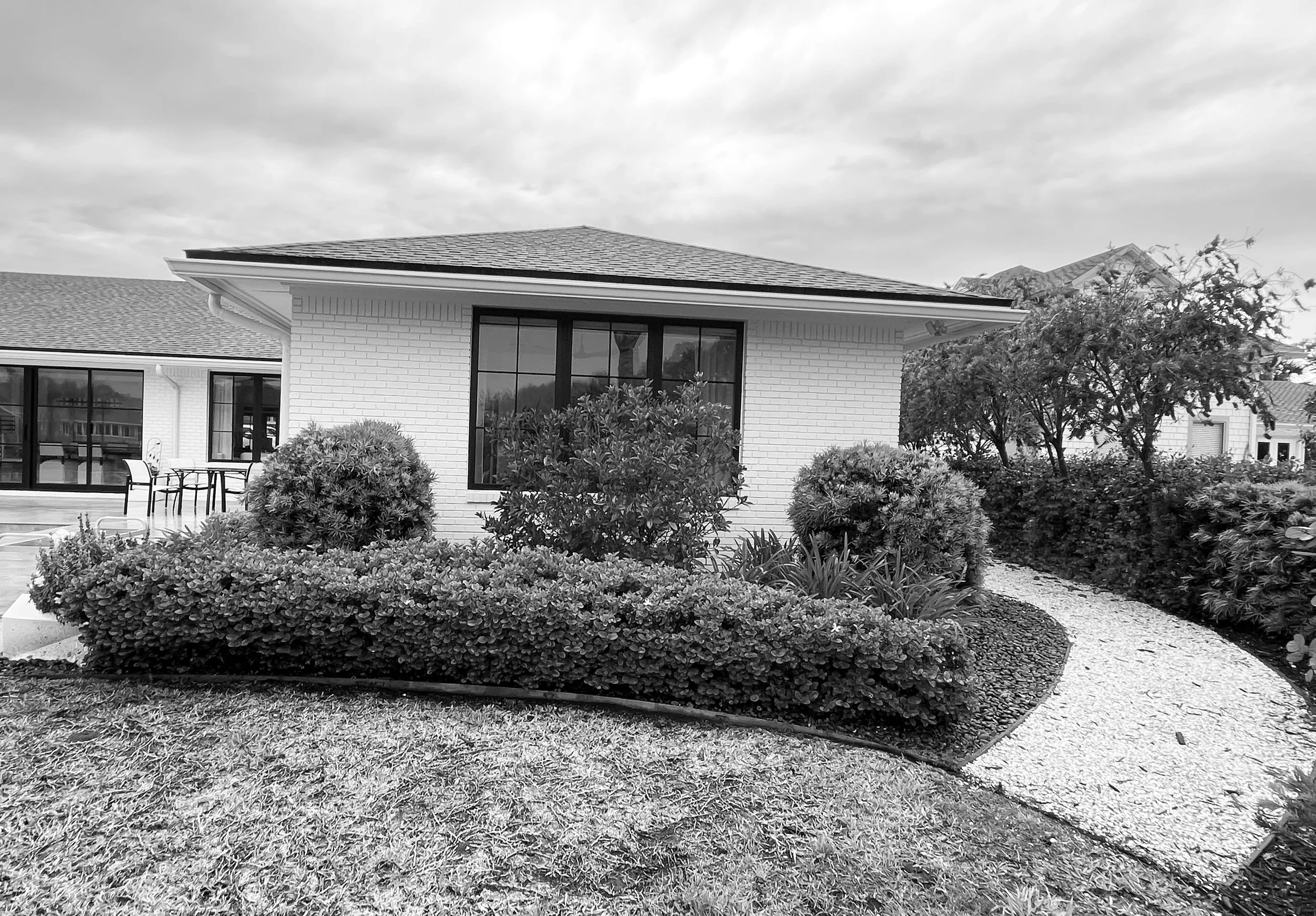 A black and white photo of a modern house with a garden featuring trimmed bushes and a gravel pathway.