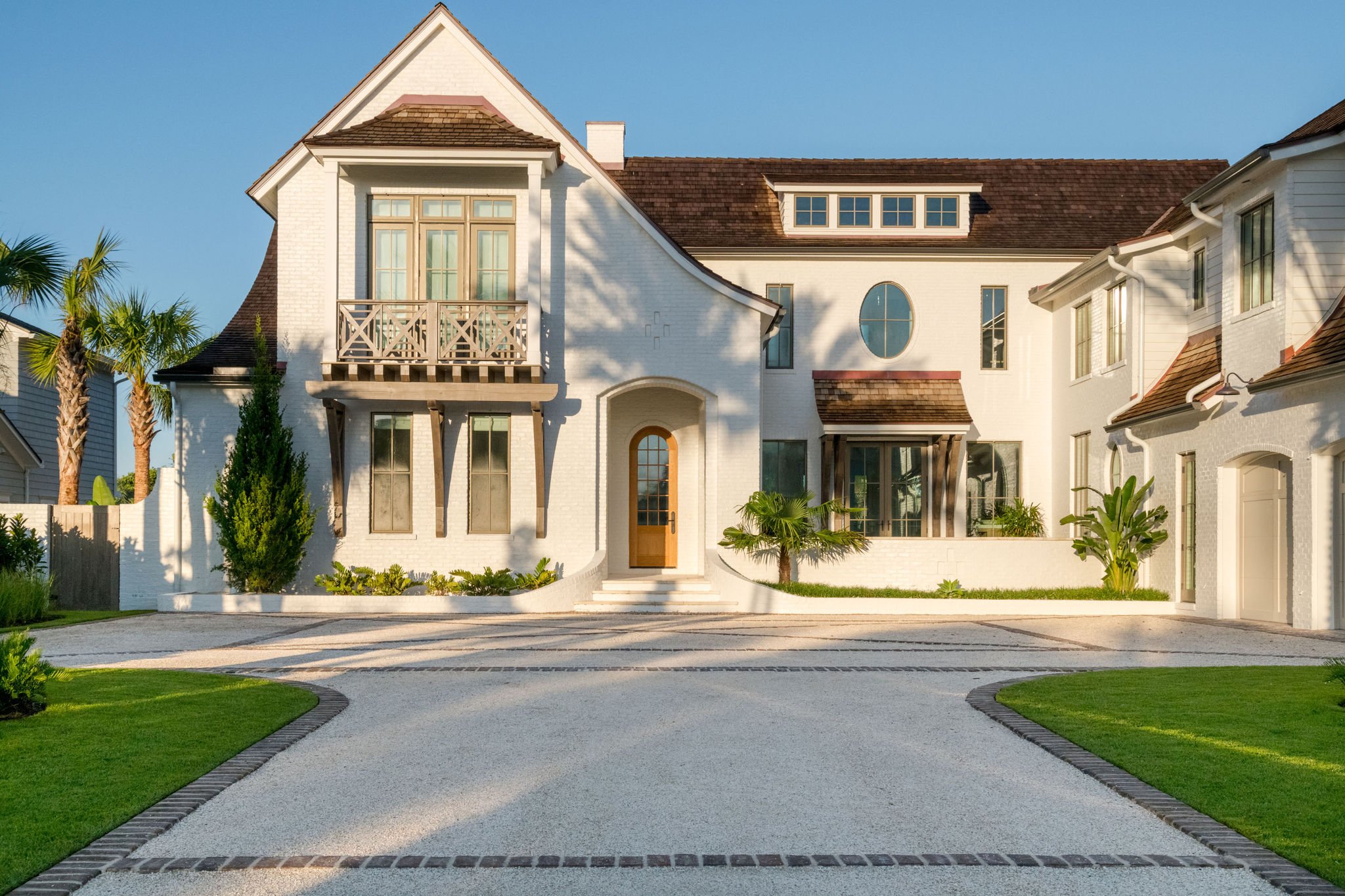 Luxury coastal residence in Ponte Vedra Beach, Florida, featuring a sweeping curved driveway with brick detailing, tropical palms, and minimalist landscape design complementing the home's white brick architecture