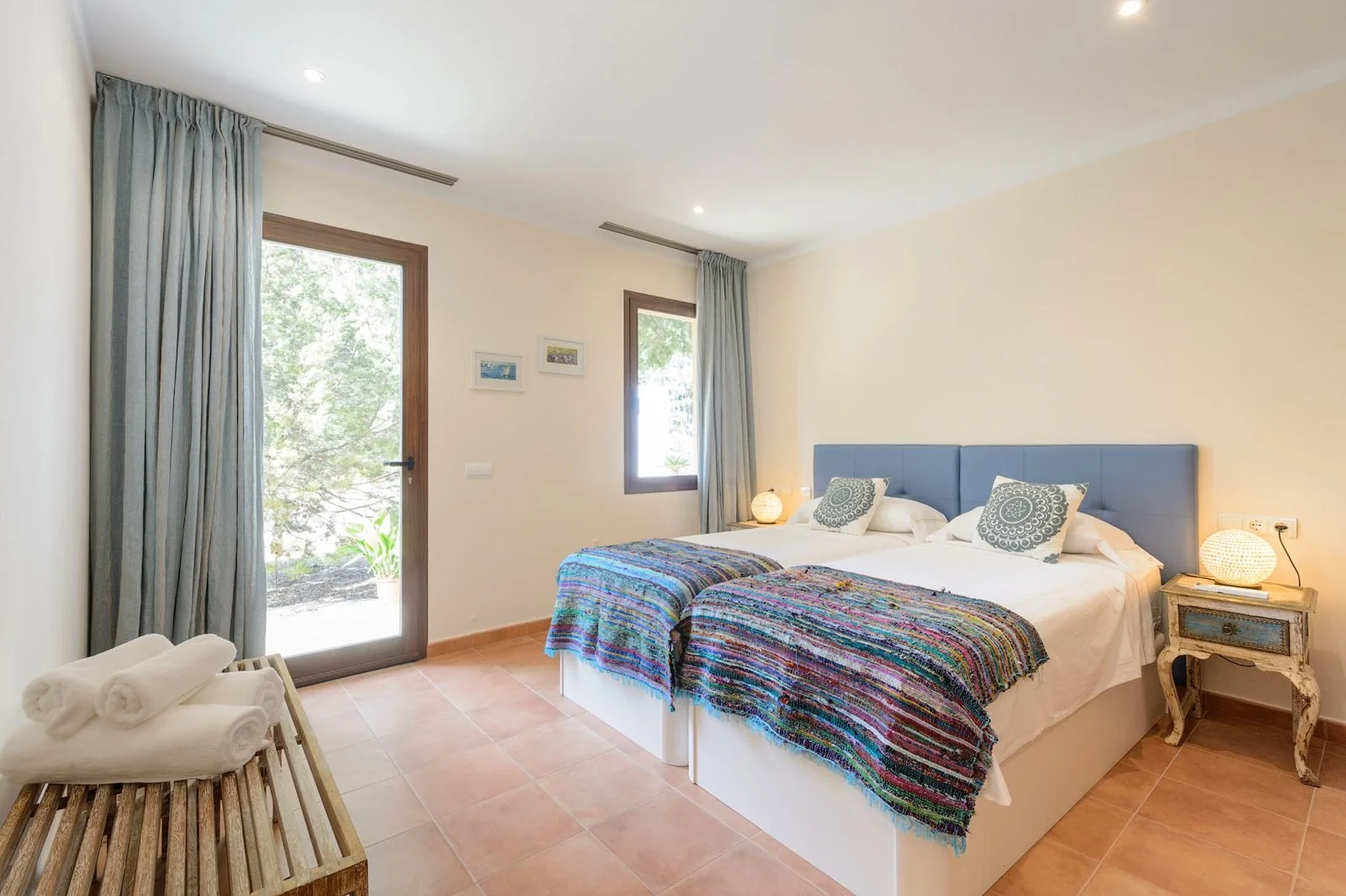 Example of a twin bedroom at our Ibiza retreat villa, with colourful throws and doors opening to the terrace.