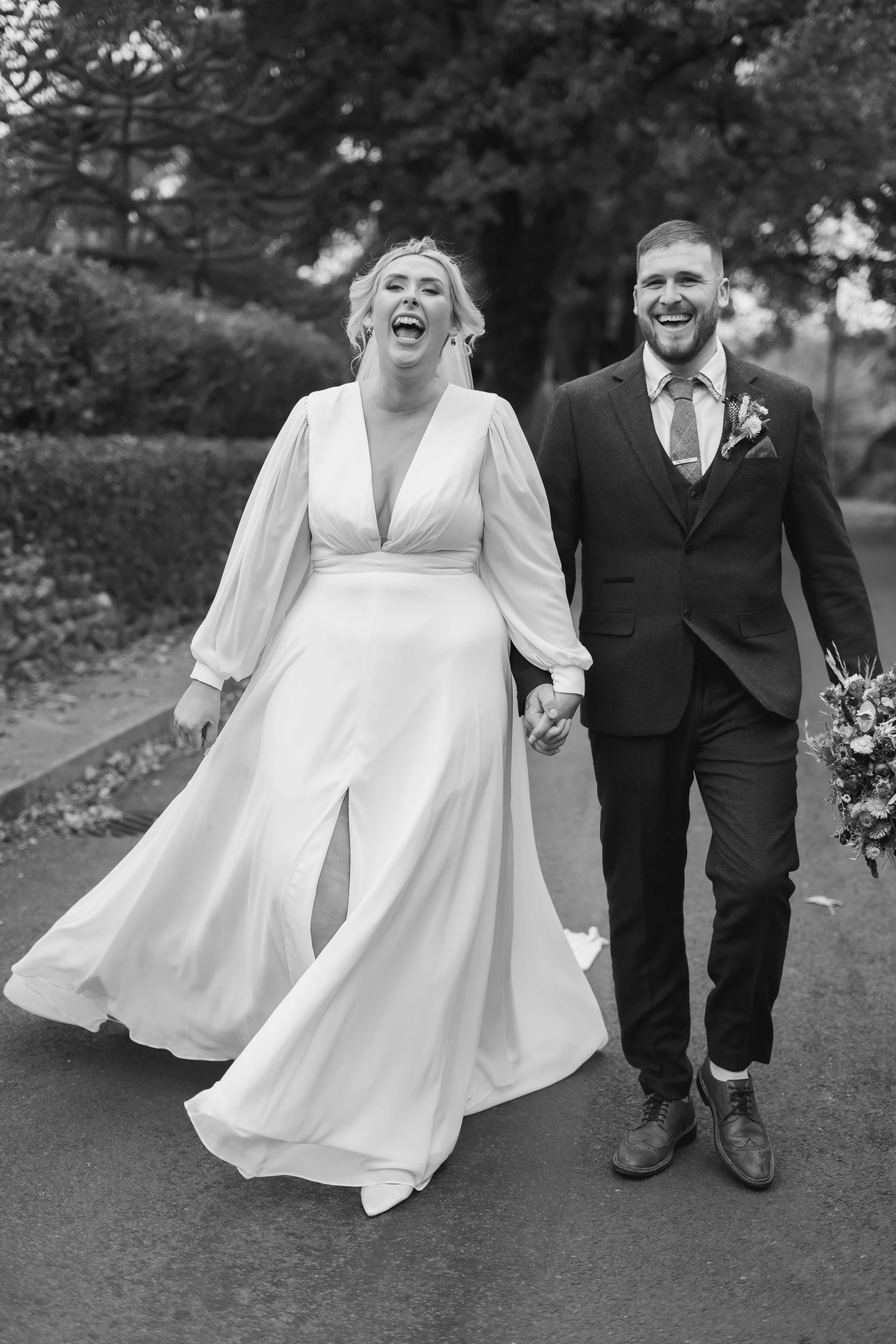 A happy bride and groom walking hand in hand outdoors during their wedding, smiling and laughing.