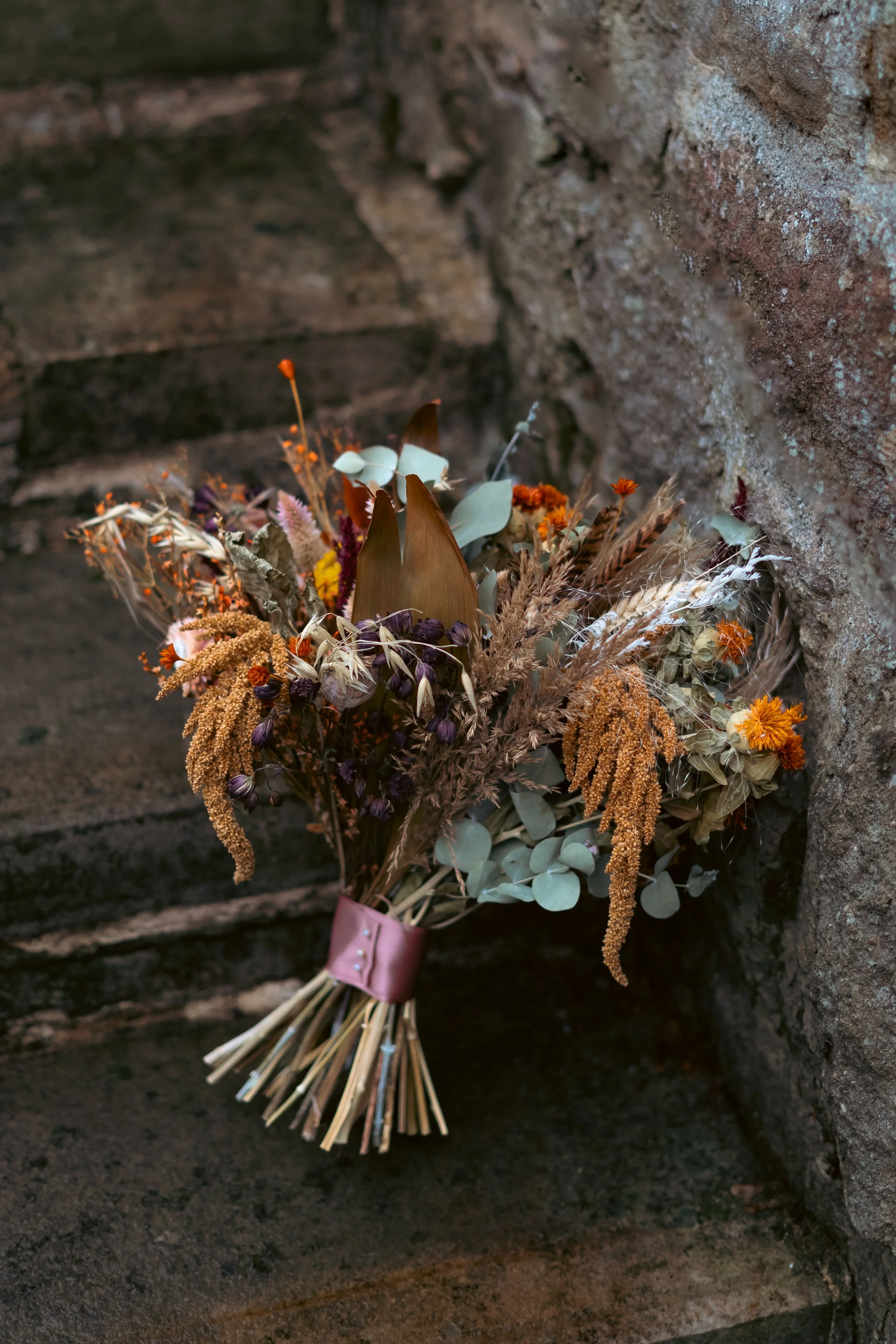 A bouquet of dried flowers leaning against a brick wall.