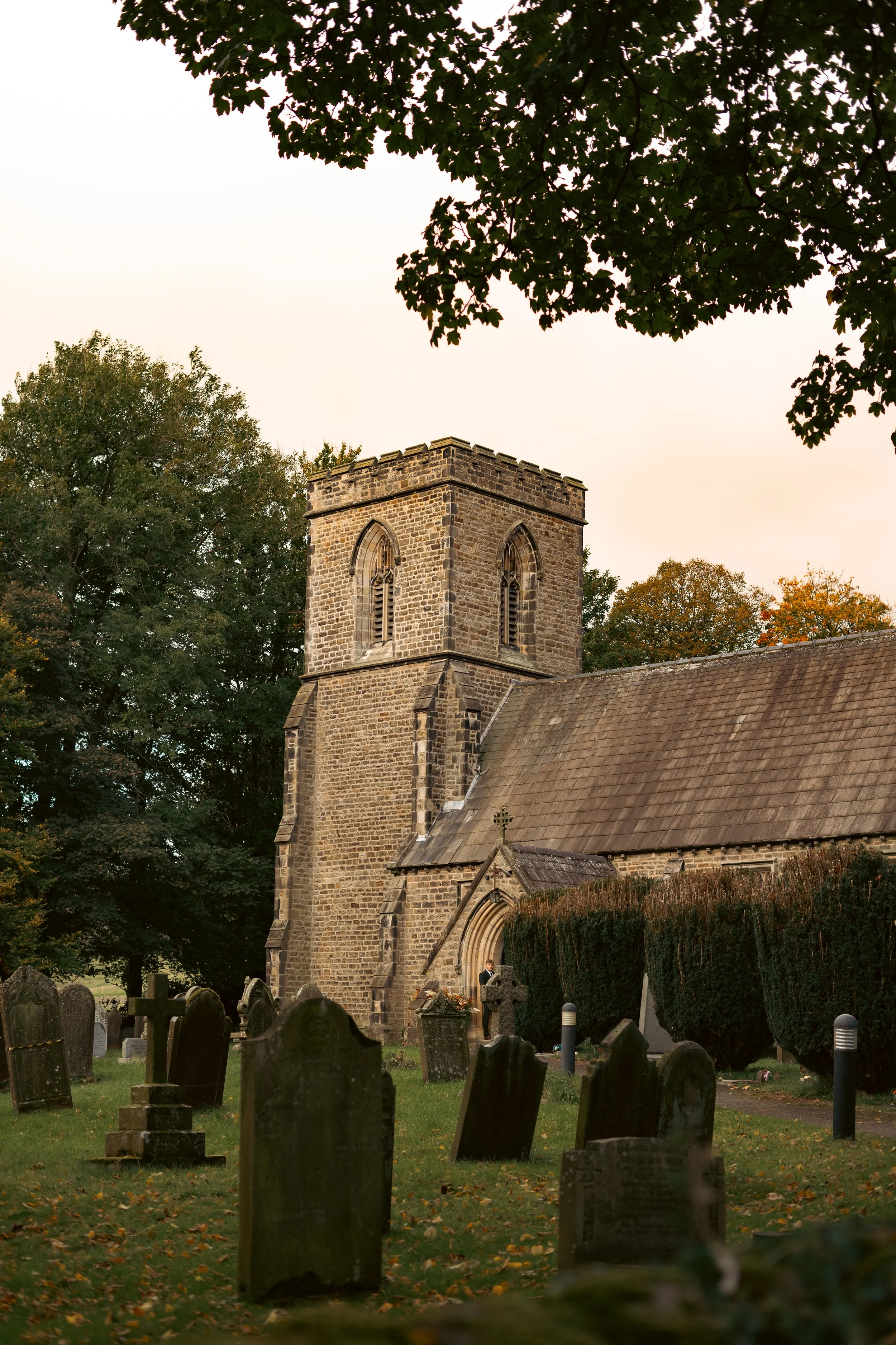 An old stone church with a square tower surrounded trees and orange autumn leaves.