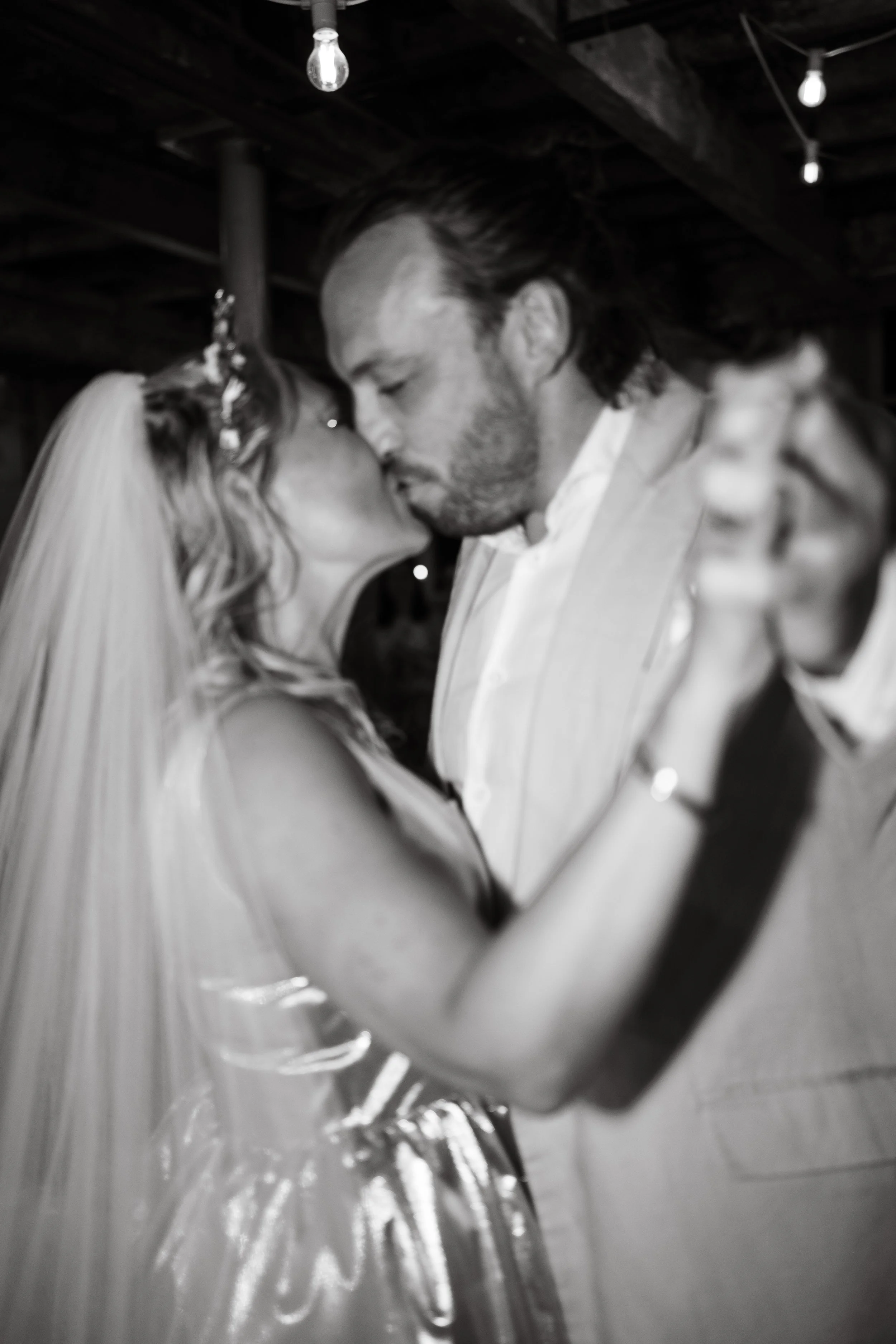 A bride and groom share a kiss during their wedding dance, with the bride in a wedding dress and veil, and the groom in a light-coloured suit at Holmes Mill