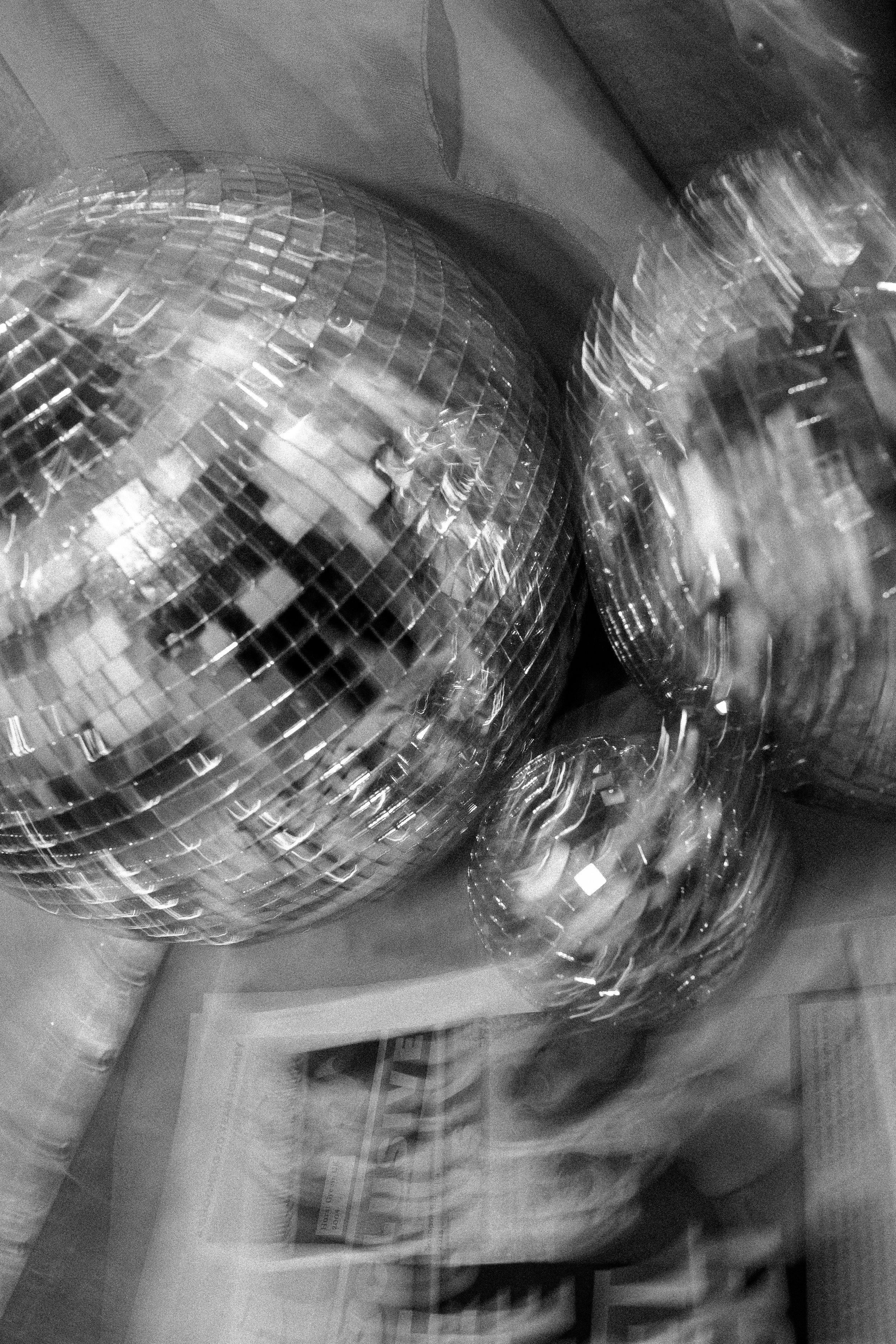 Three disco balls resting on a surface alongside a newspaper.