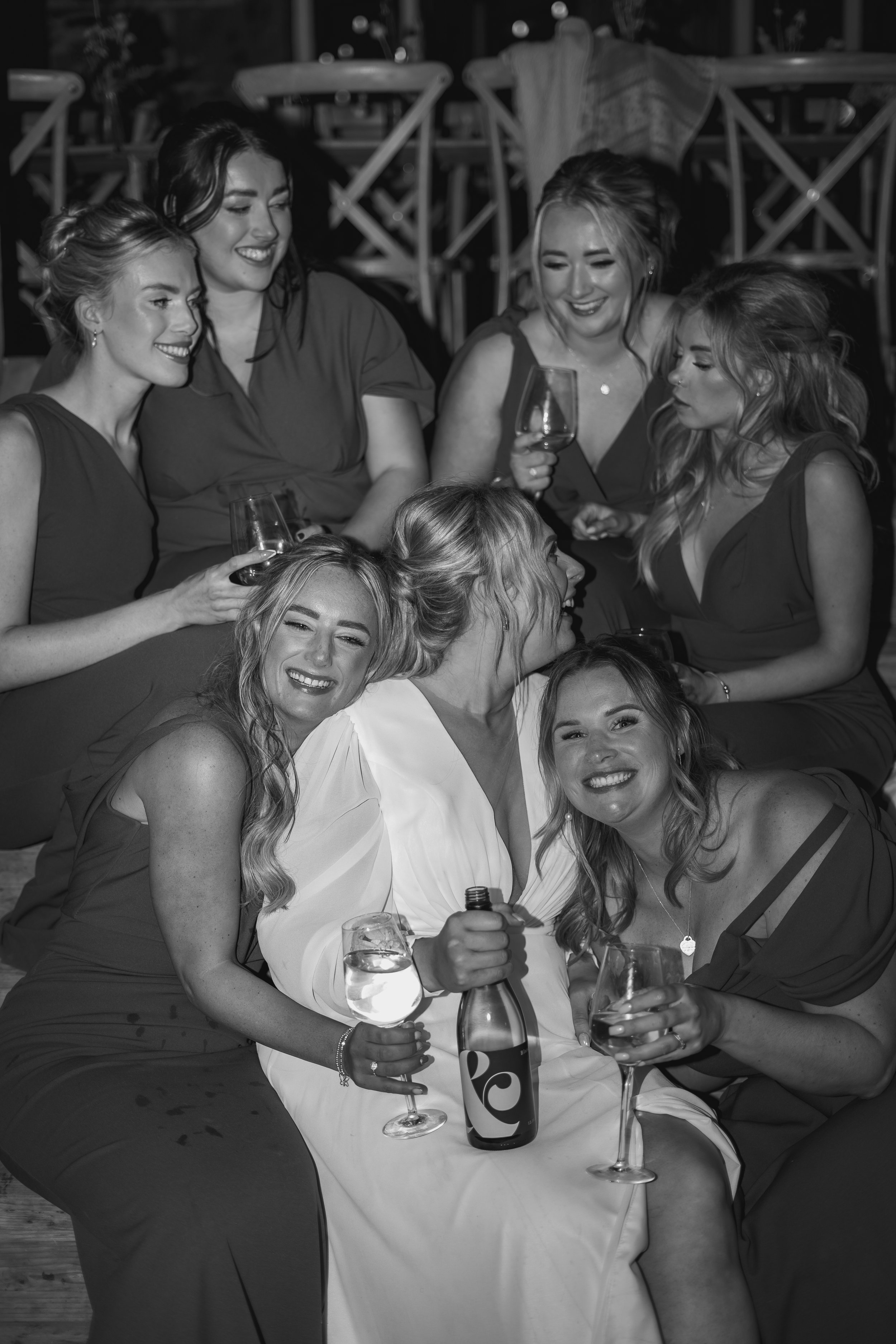 Black and white photo of a group of women enjoying drinks at a wedding, smiling and chatting together.