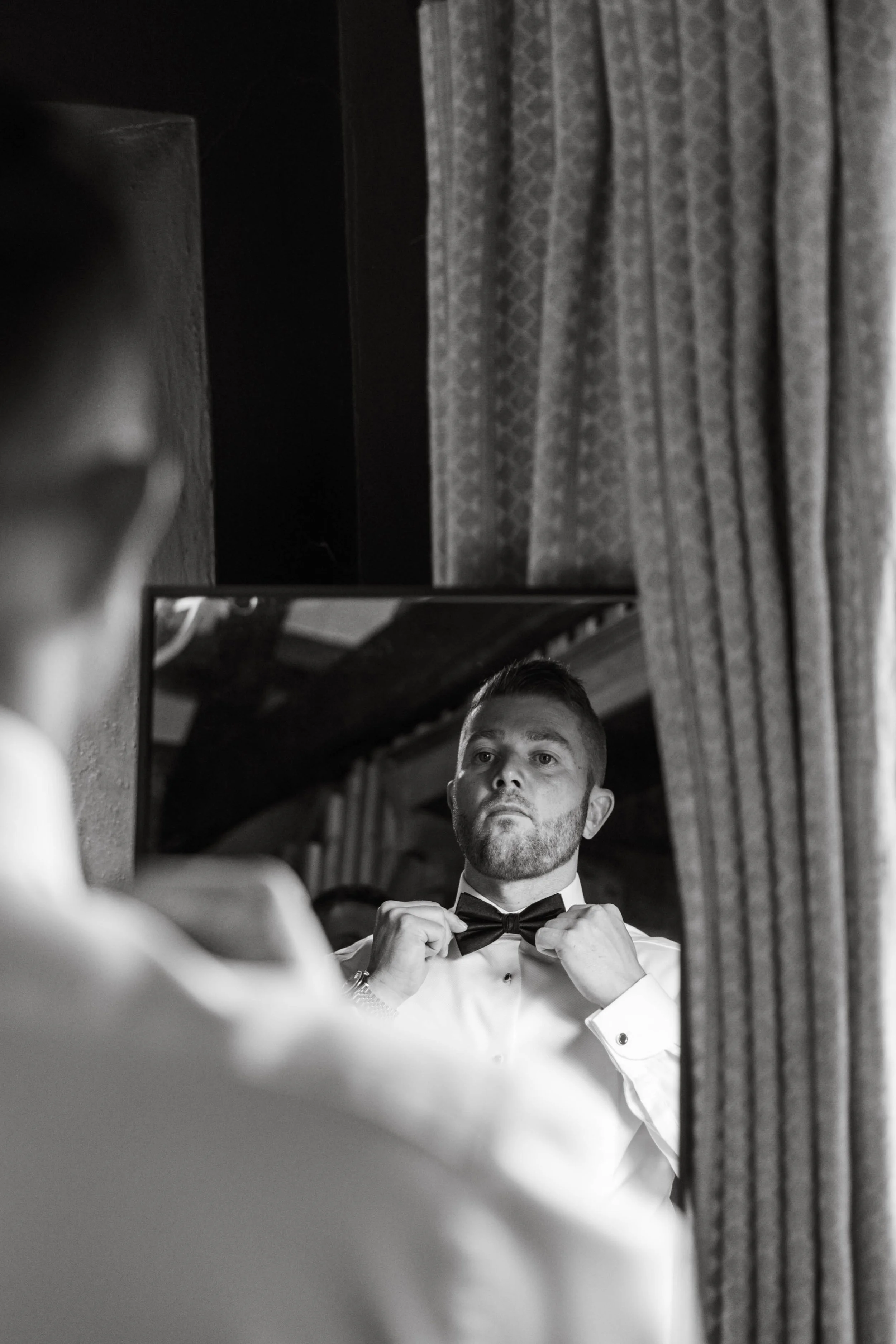 Groom adjusting bow time in front of mirror at Askham Hall