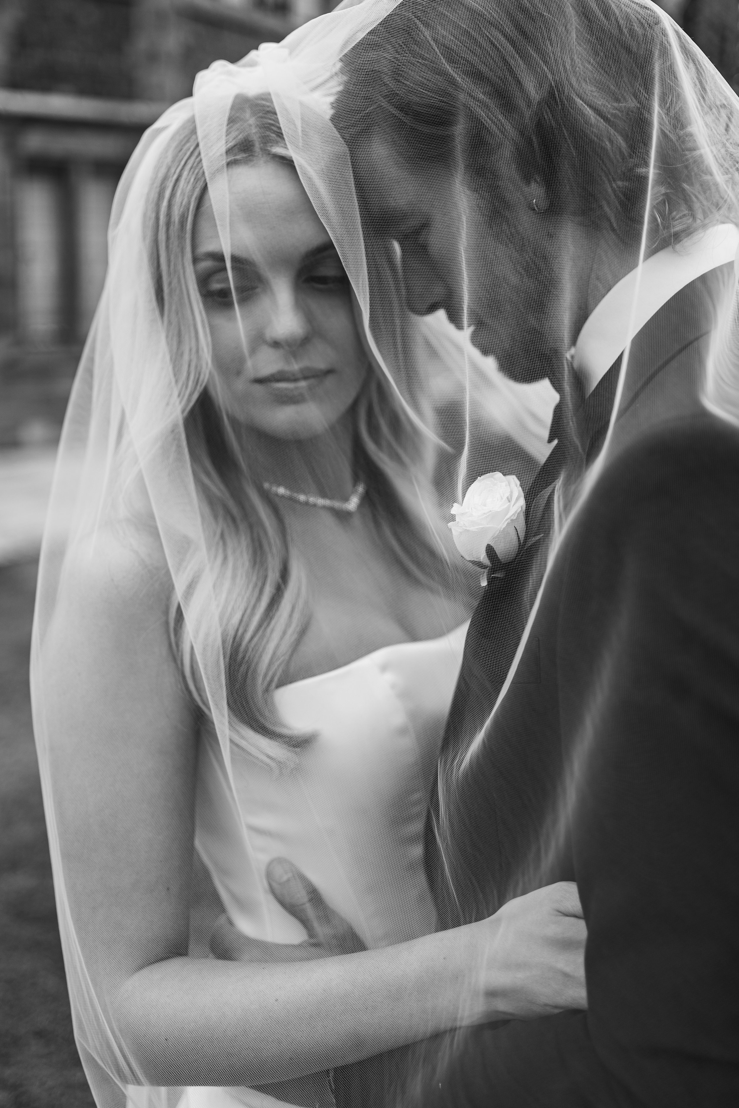 Black and white photo of a bride and groom with their foreheads touching, under the bride's veil during wedding.