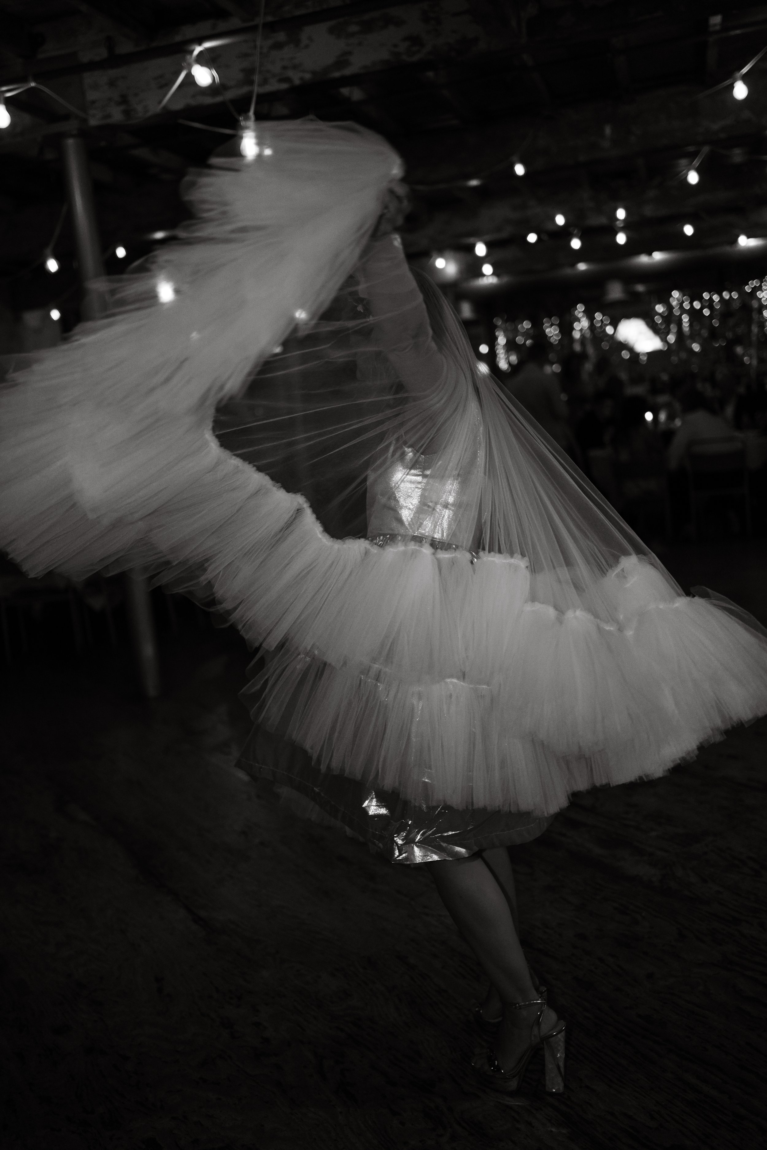 A woman dancing in a flowing dress under string lights at an indoor event.