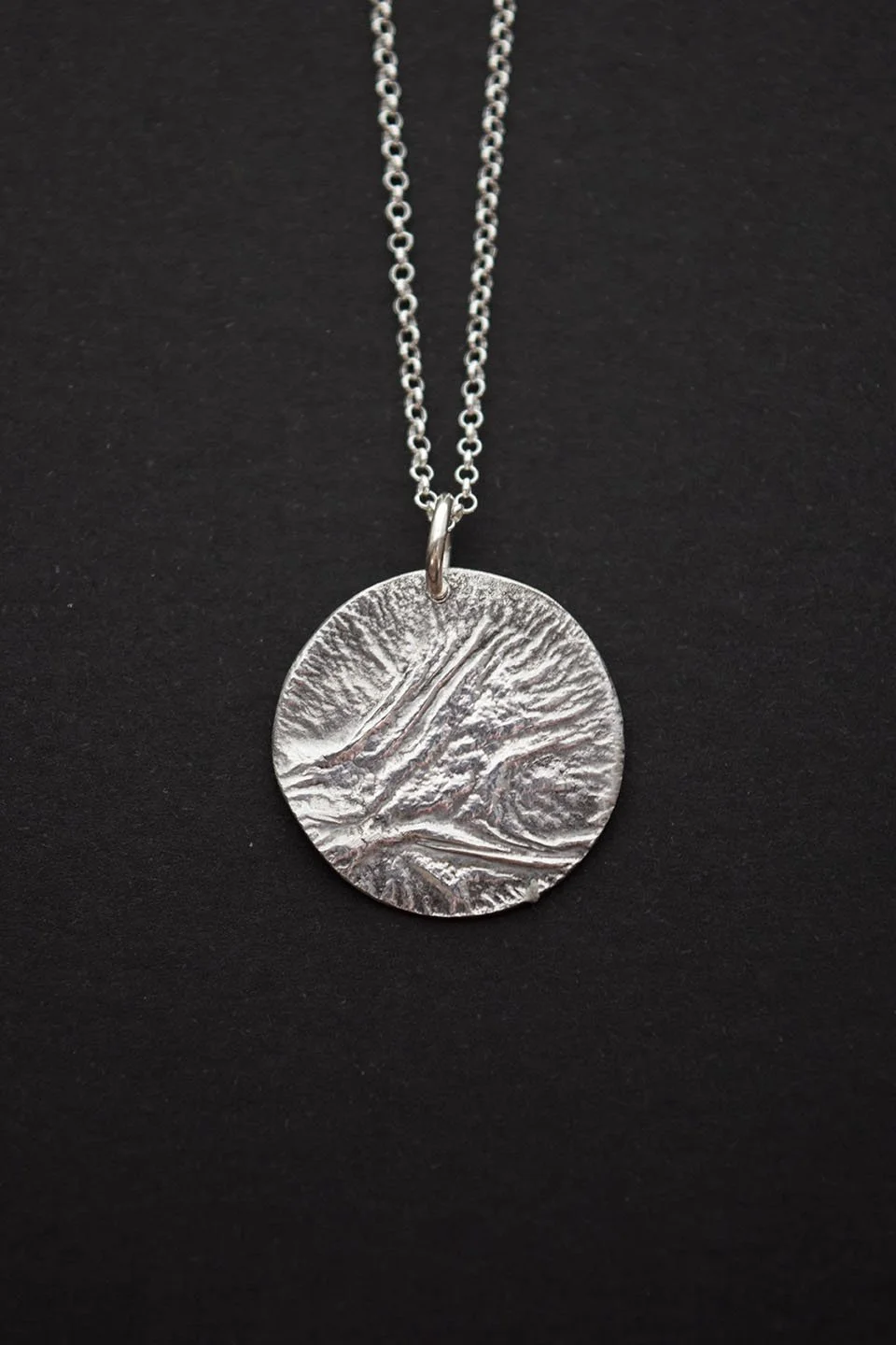 Silver necklace with a large textured round pendant on a black background.