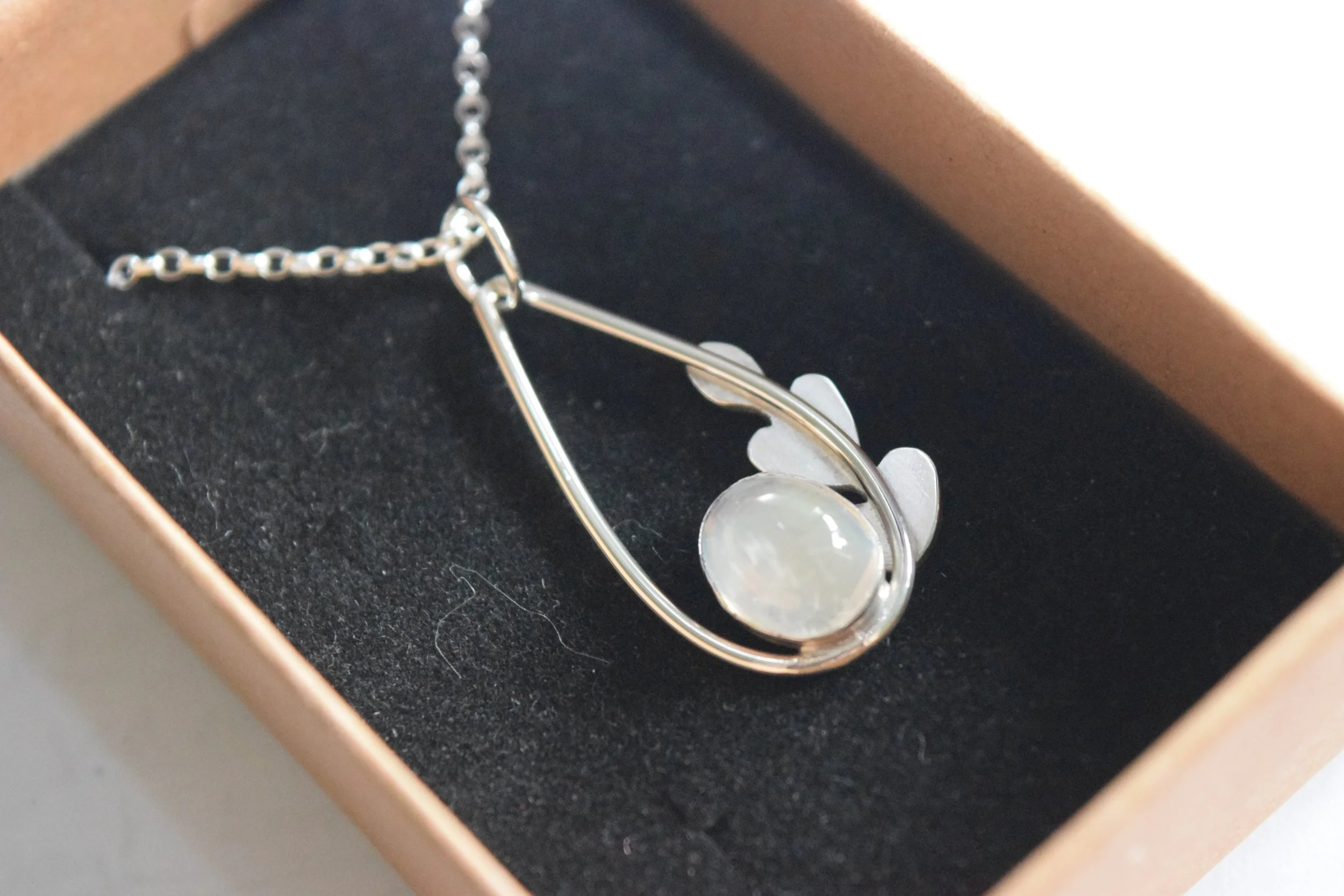 Silver necklace with circular and flower-shaped charms inside a black jewelry box.
