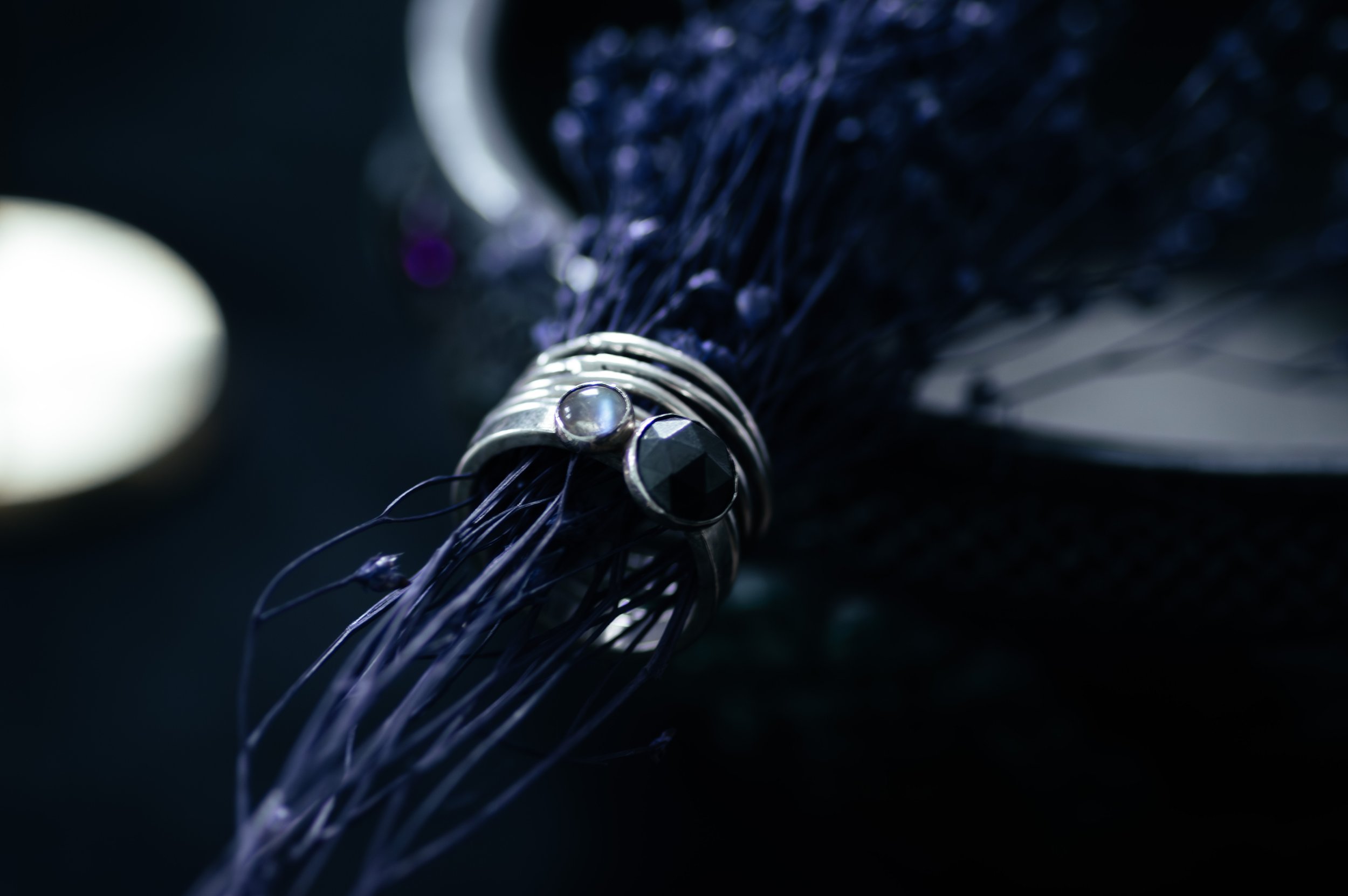 Close-up of a jewelry piece, featuring a silver ring with a black gemstone, wrapped around dark-colored thread or wire.