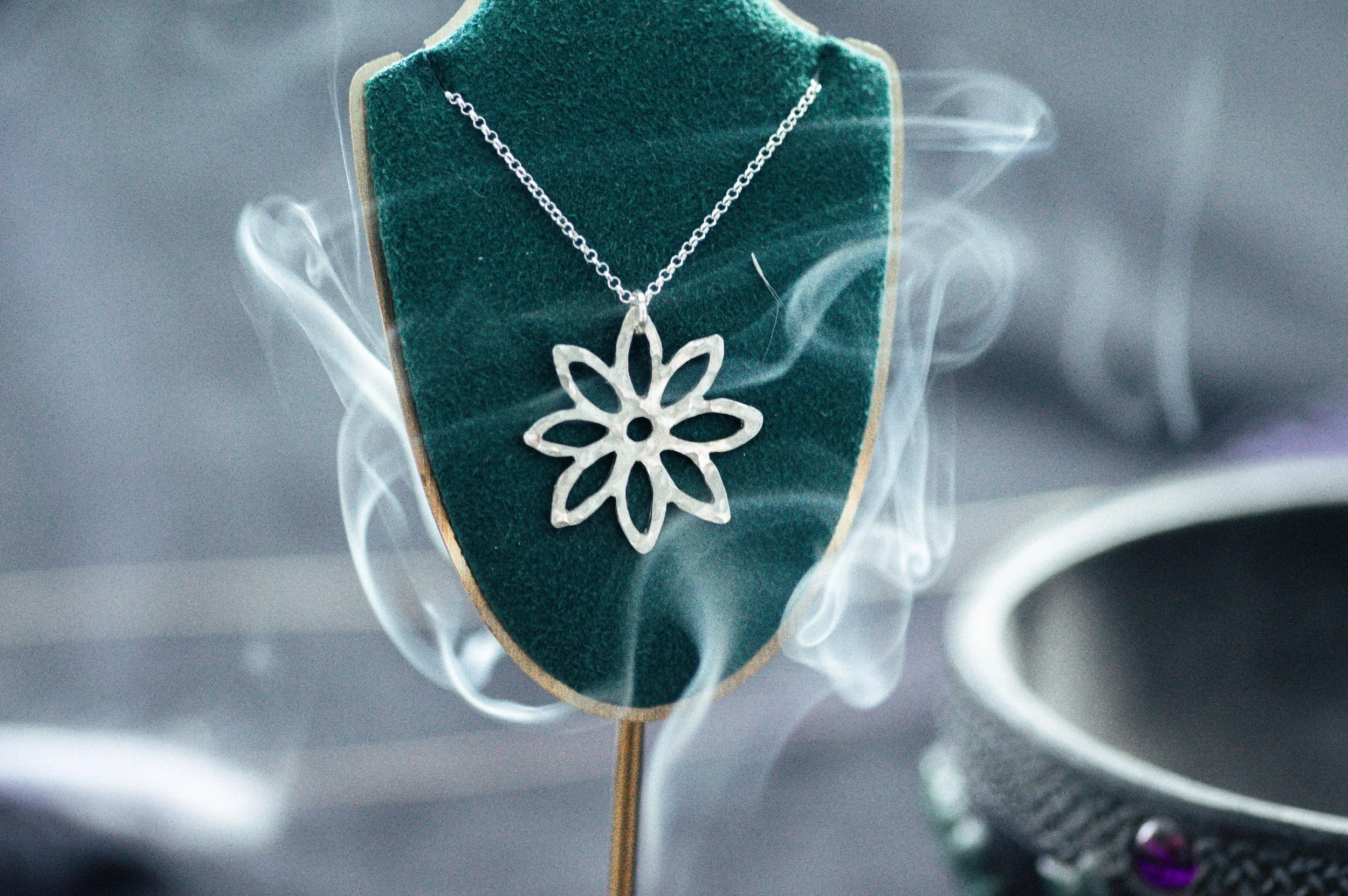 Silver necklace with a flower-shaped pendant displayed on a green velvet necklace holder.