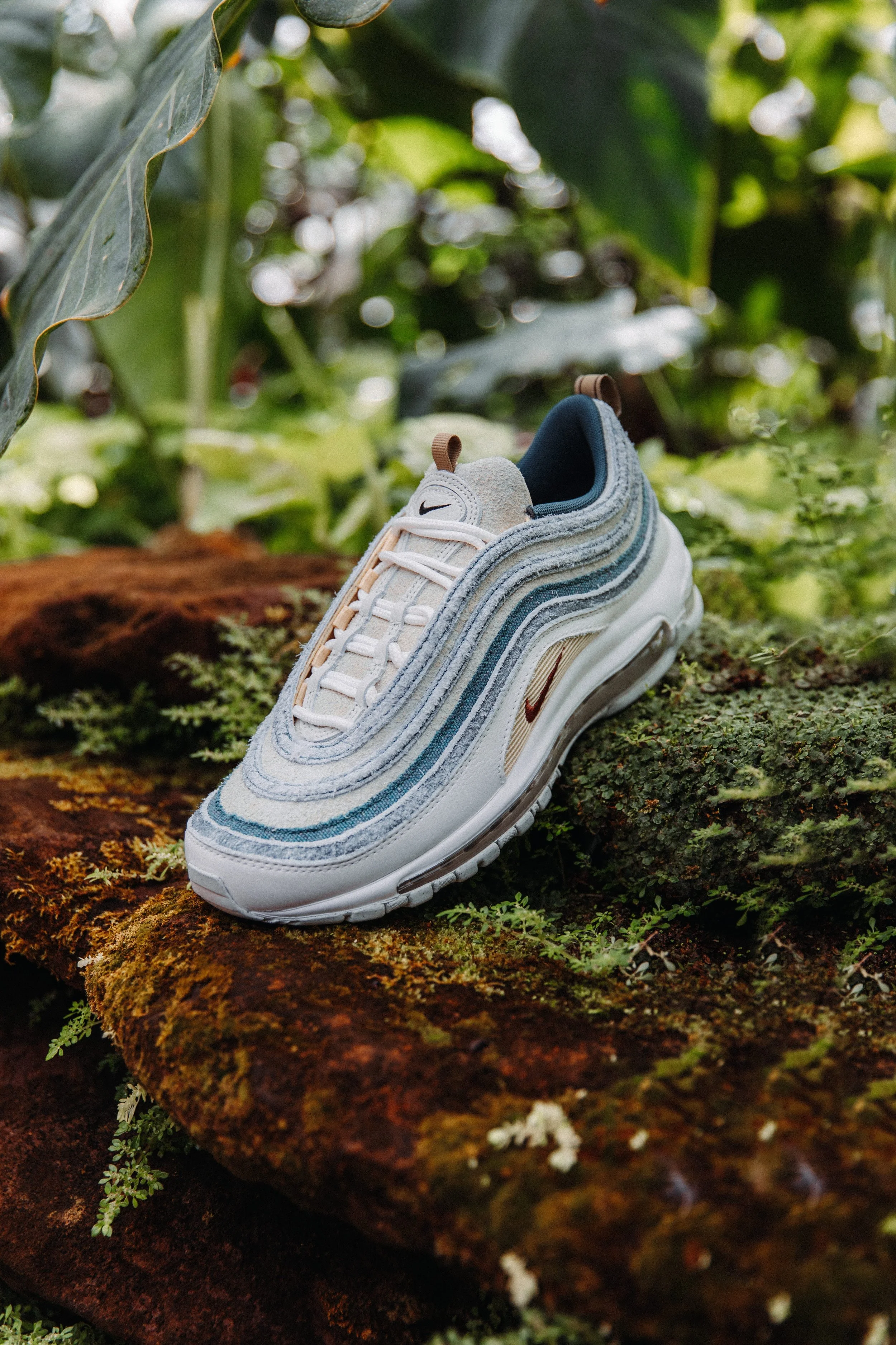 A Nike Air Max sneaker resting on a moss-covered log surrounded by green foliage.