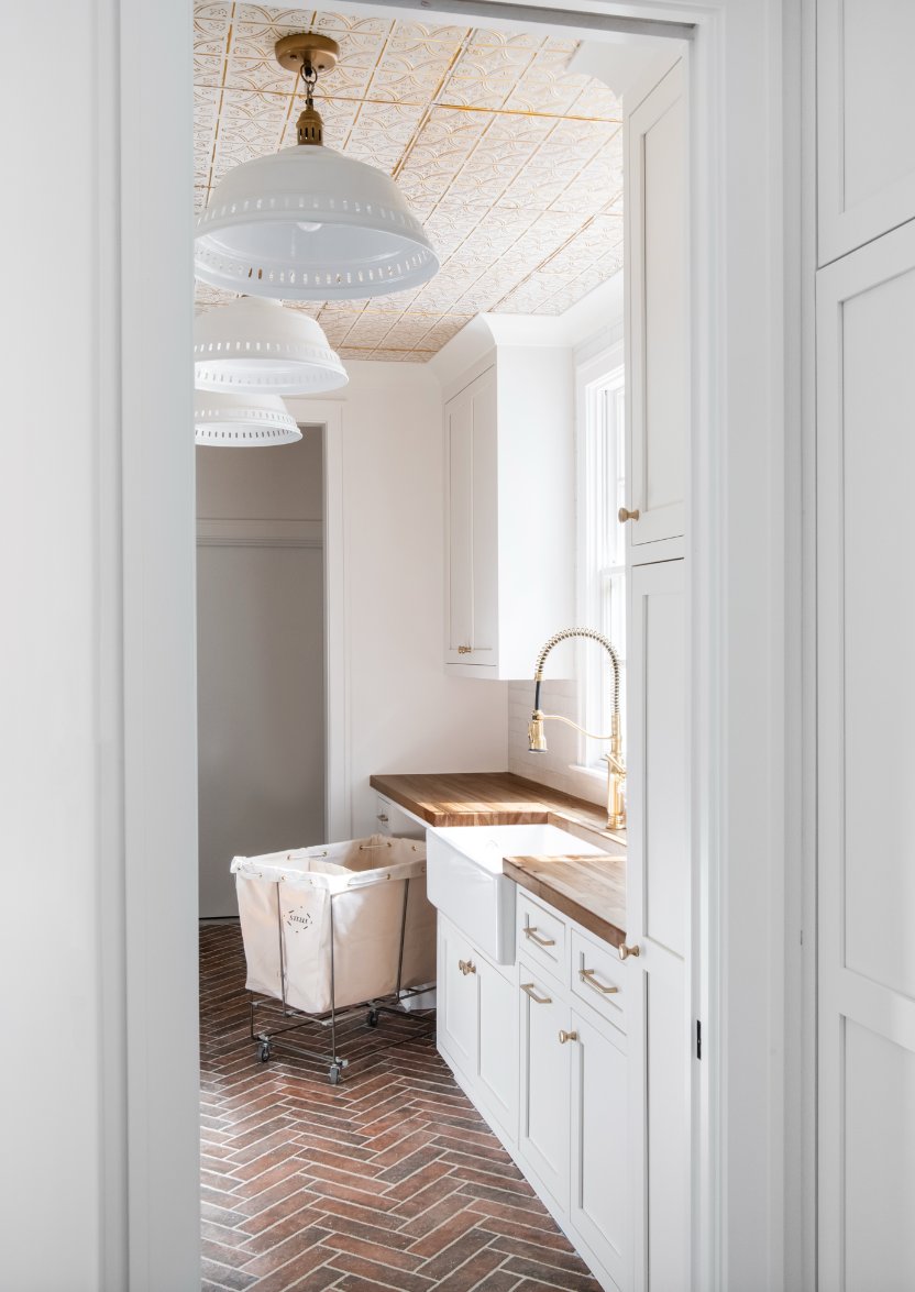 Farmhouse laundry room in Nashville custom home with white cabinets, brick floor, and butcher block counters.