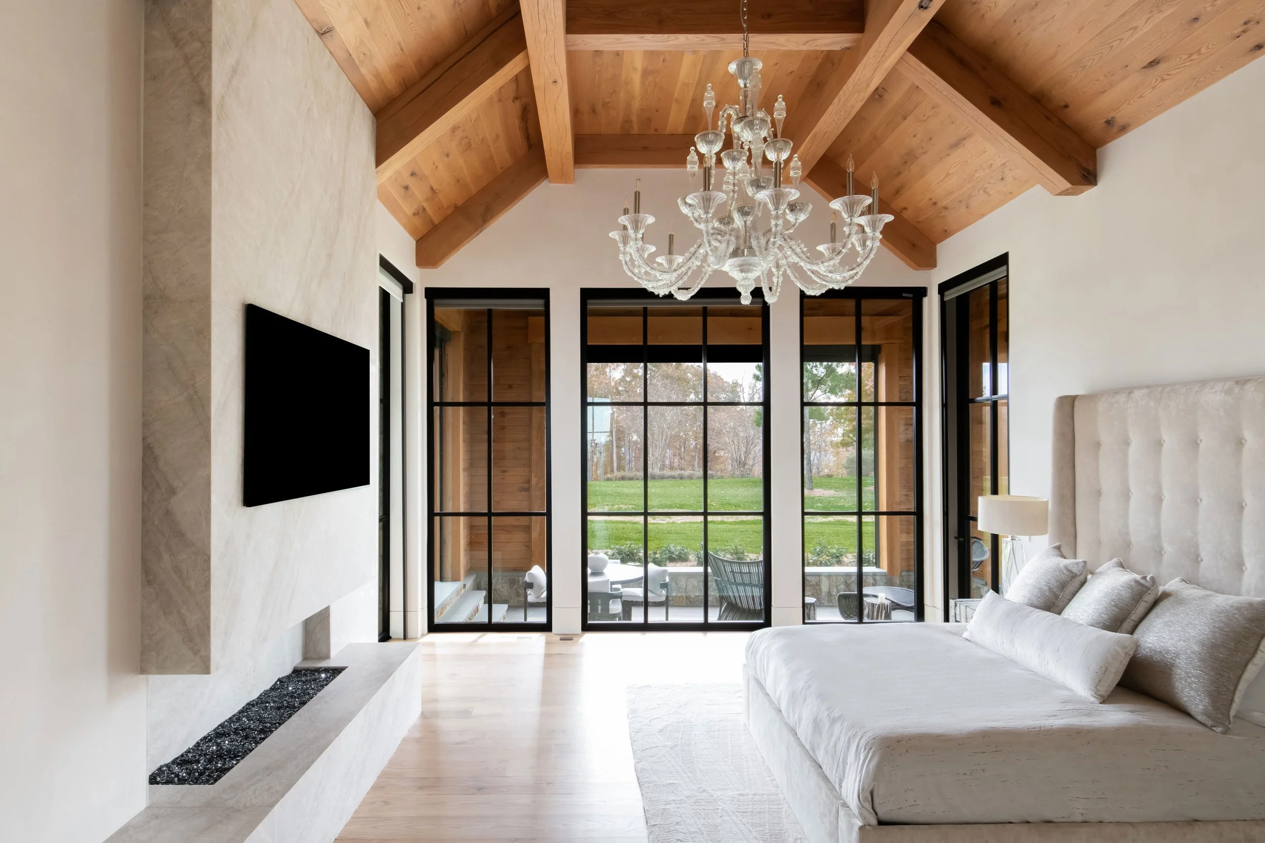 Luxury bedroom with fireplace, chandelier, and black frame windows. Custom home Nashville.