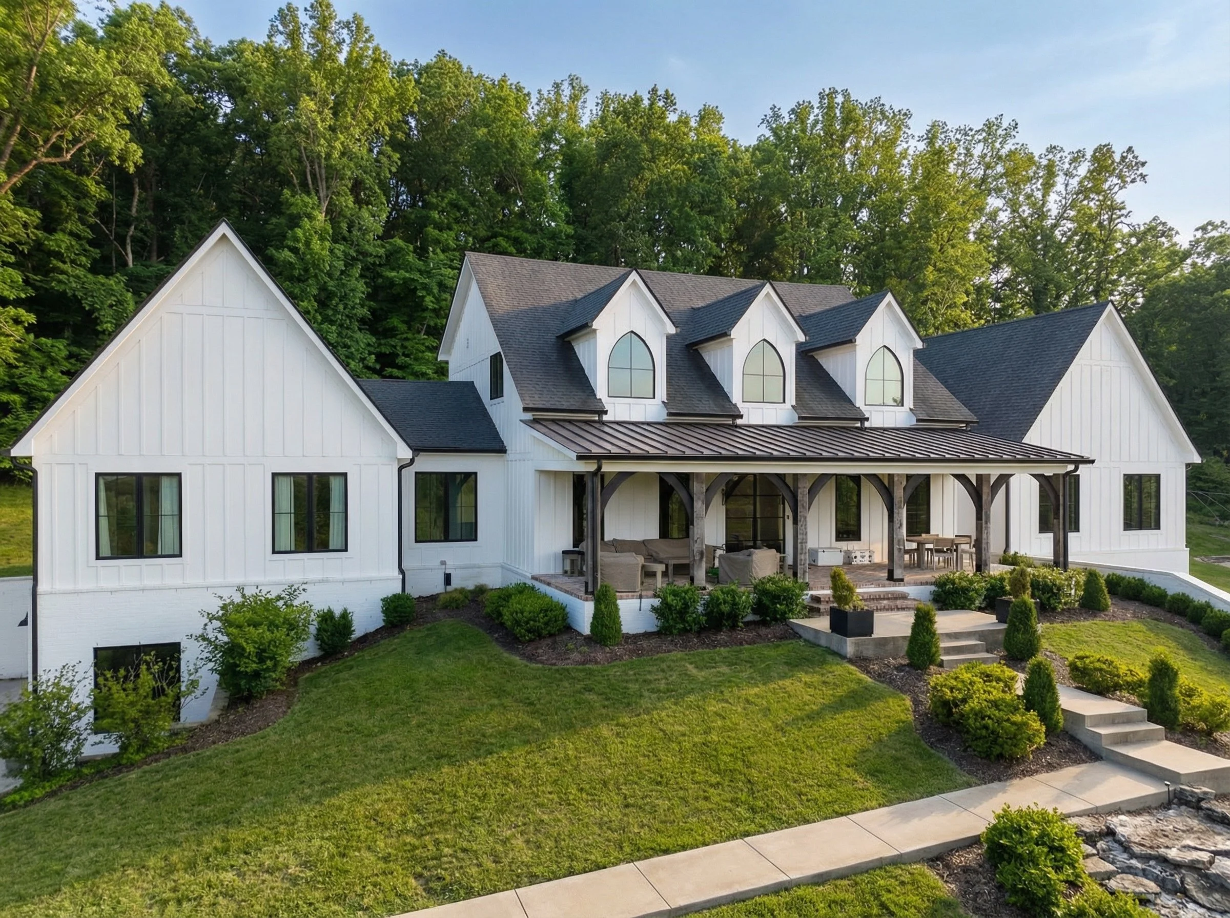 Exterior of a white modern farmhouse by a luxury home builder Nashville. Dark windows, front porch.
