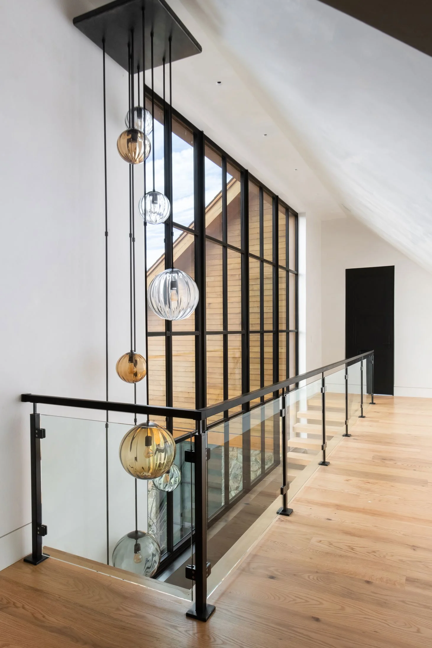 Modern hallway with globe pendant lights and large black-framed window. Custom home Nashville.
