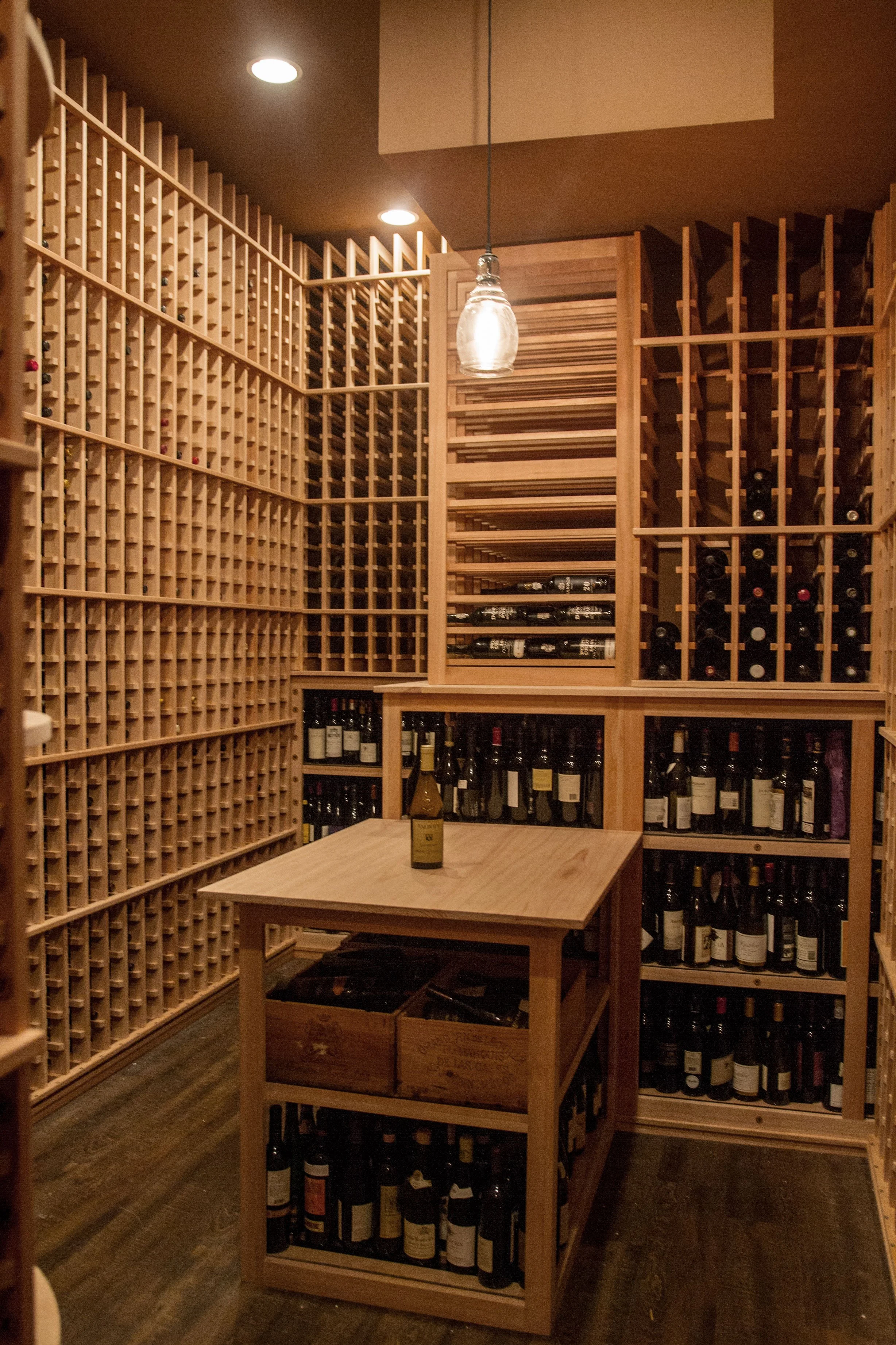 A walk-in wine cellar with wooden shelves filled with wine bottles, a small wooden table with a single wine bottle on top, and a hanging light fixture.