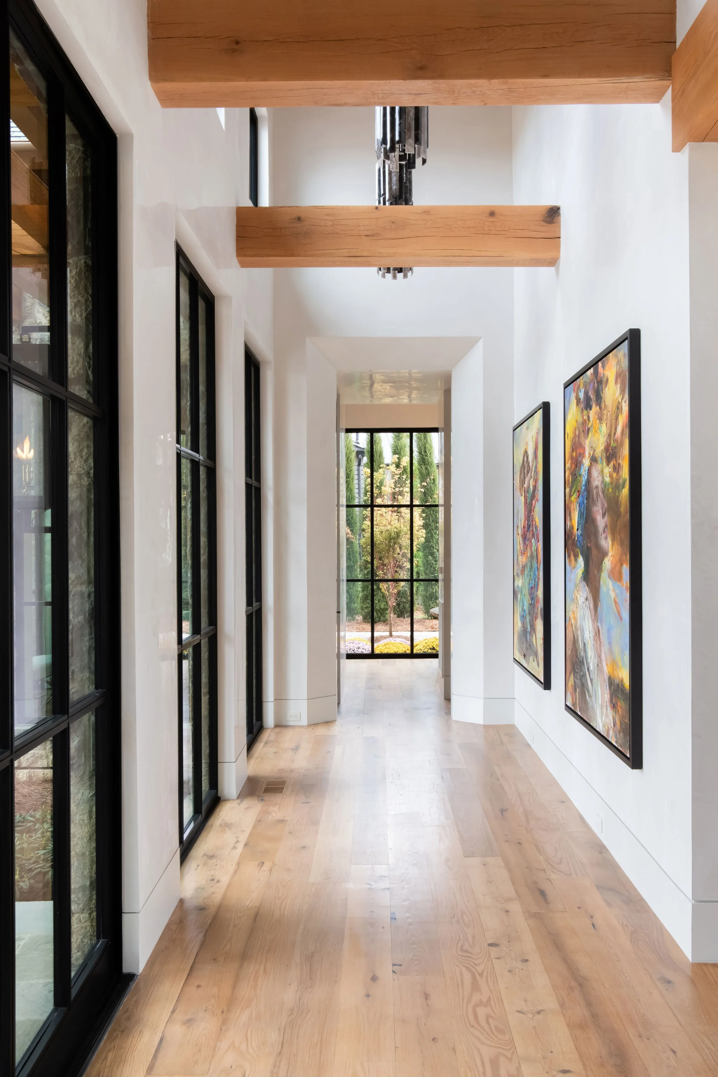 Hallway in custom home Nashville featuring wooden beams, artwork, and black-framed windows.