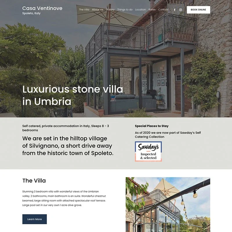 Exterior view of Casa Ventinove, a luxurious stone villa in Umbria, Italy, showing a modern glass extension with outdoor balcony, surrounded by greenery.