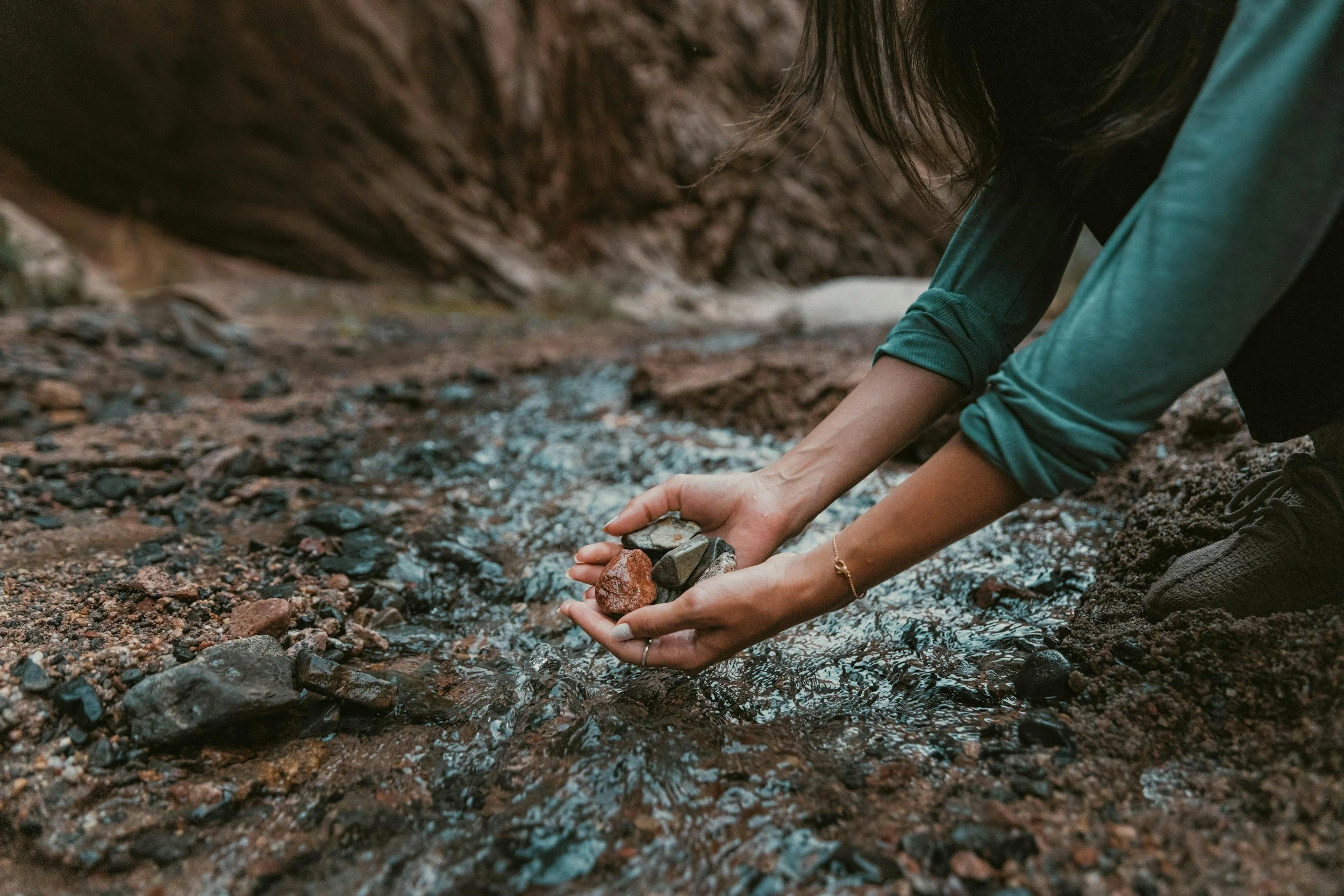 Person collecting small rocks and pebbles from a shallow stream in a natural outdoor setting.