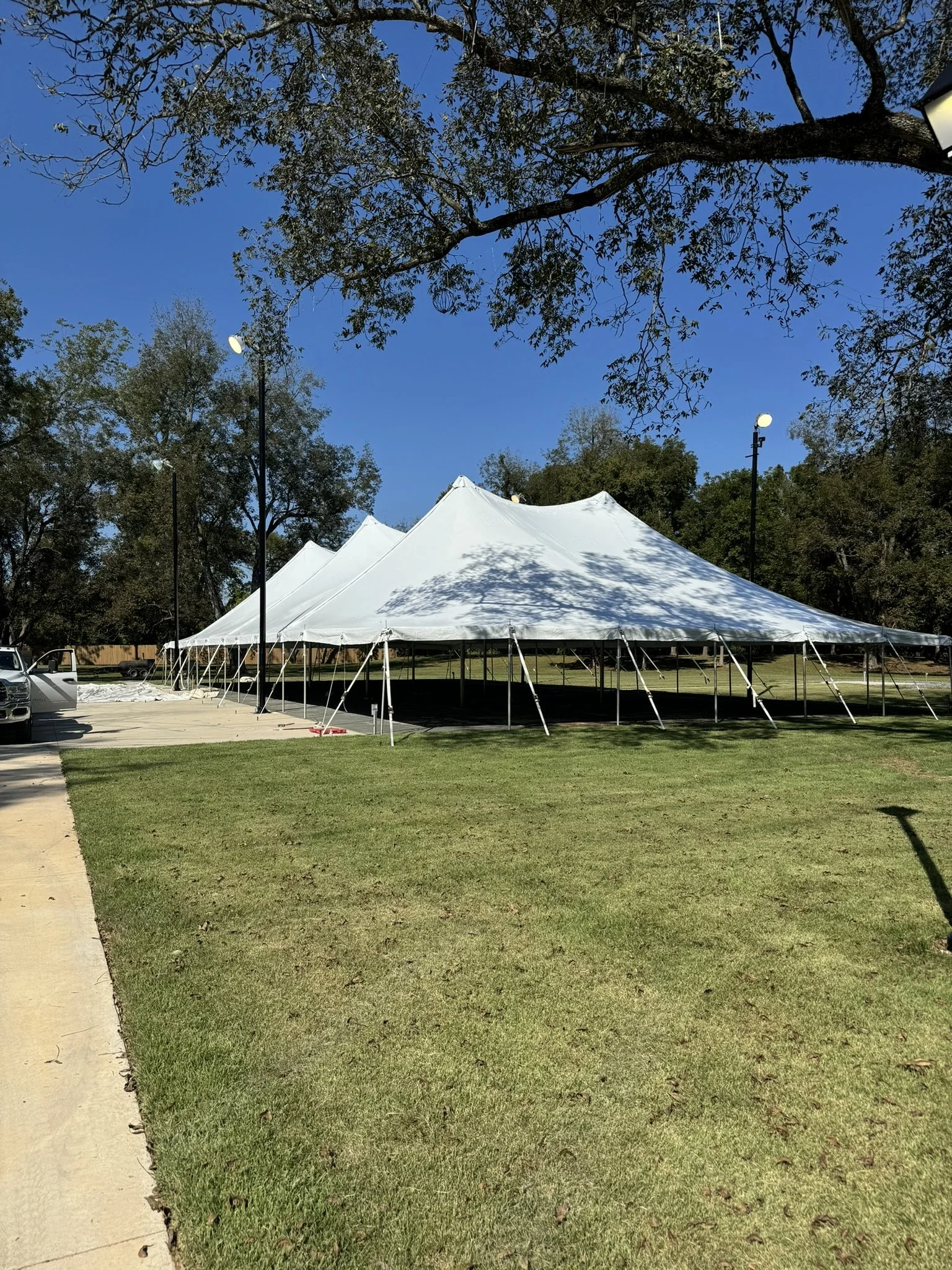 Large white event tent set up outdoors on a grassy area with trees and a blue sky in the background.