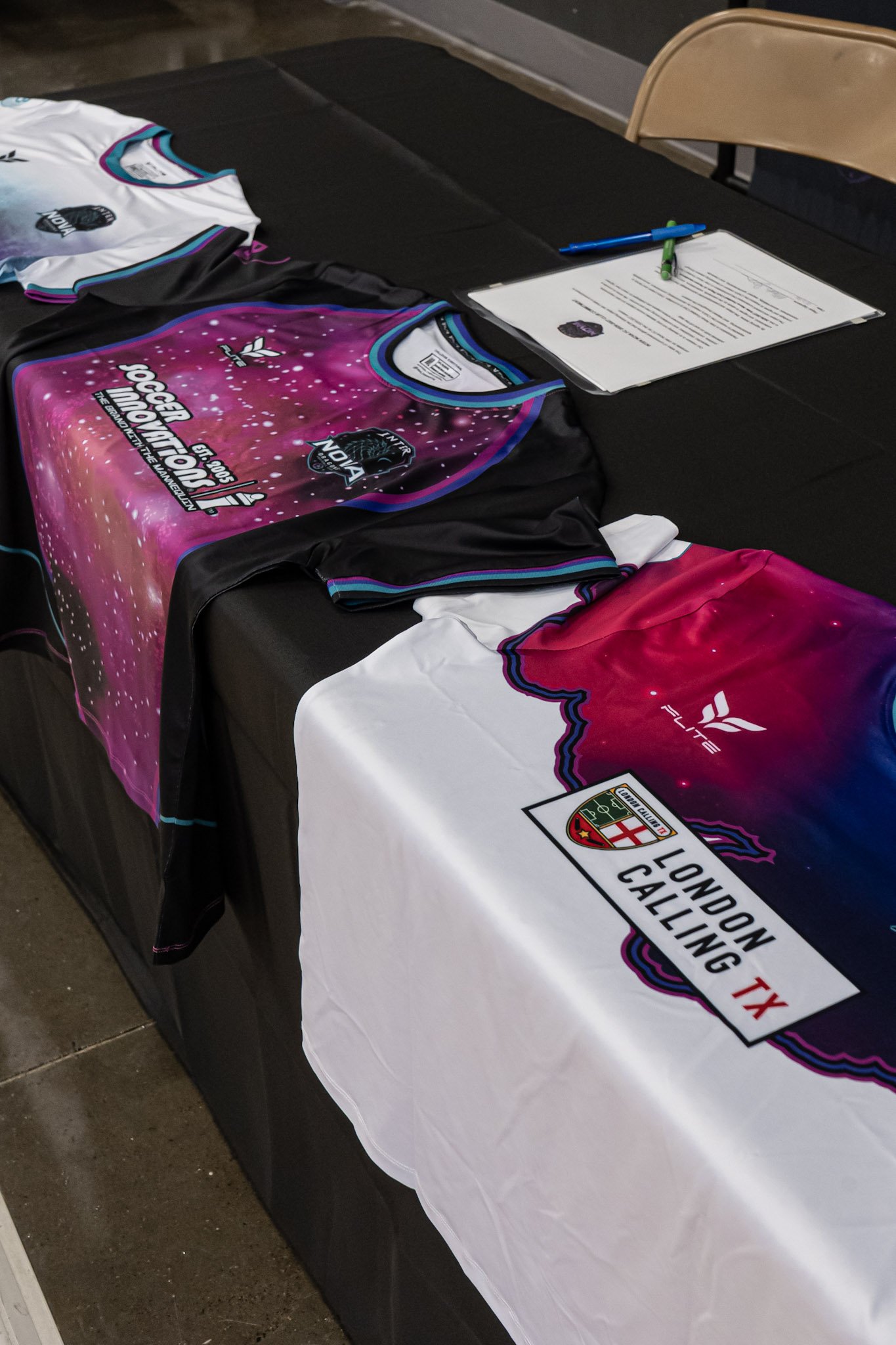Table with a folded sports jersey and a banner for the London Calling event. The jersey is black, pink, and white with logos, and the banner is black and white with red accents, featuring text and a crest.