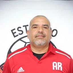 A man with a bald head and beard wearing a red shirt stands in front of a white background with black text and logo.