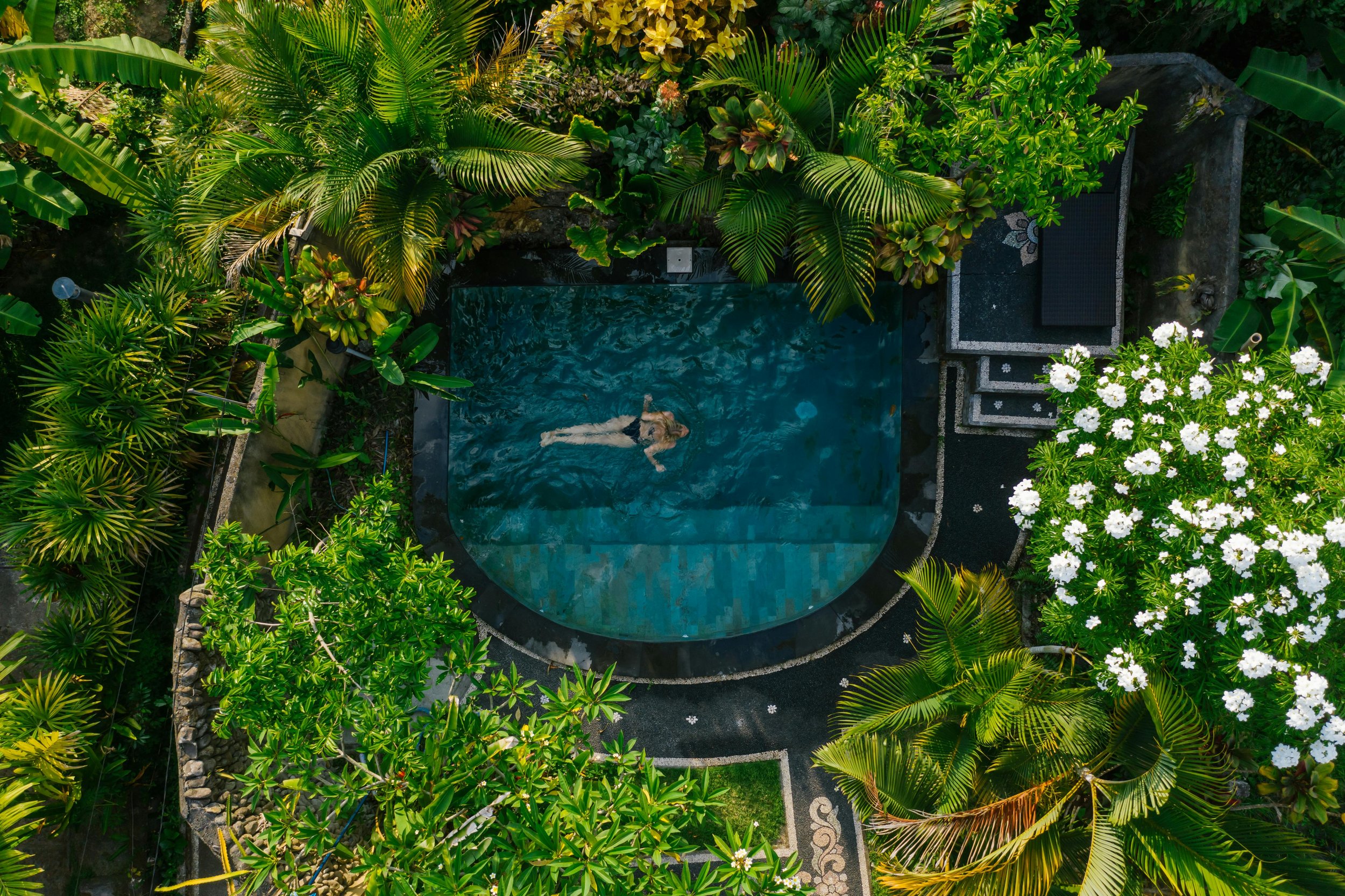 Aerial view of a woman relaxing in a private luxury infinity pool surrounded by tropical gardens