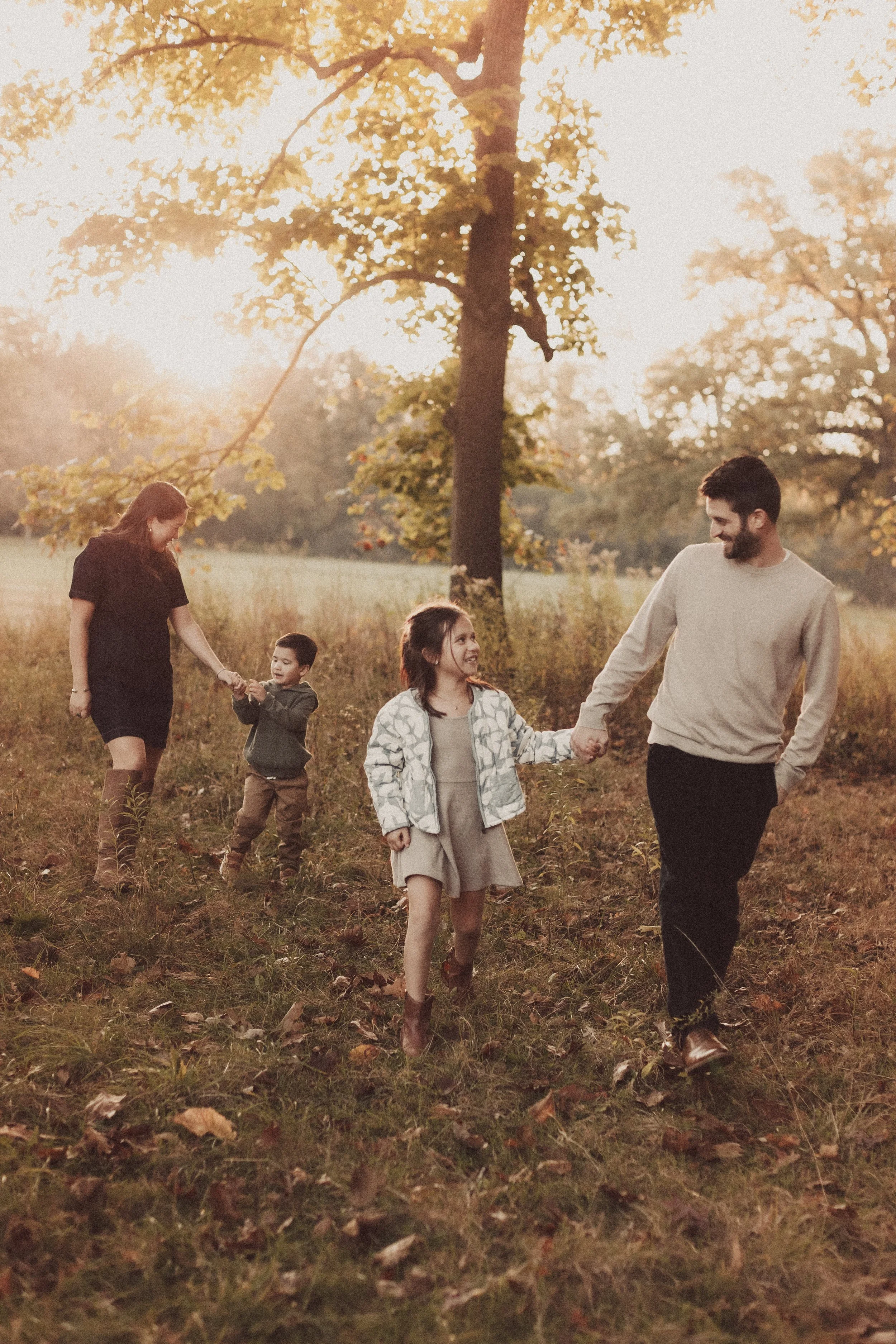 father and daughter holding hands walking and talking and mother and son in background.  Park session in fall