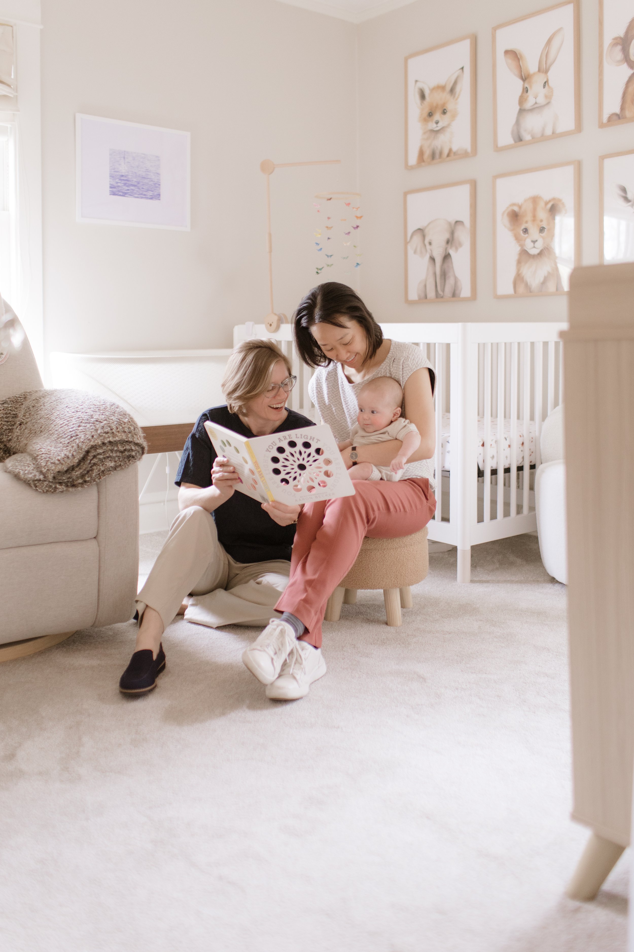 A woman, an older woman, and a baby sitting on the floor of a nursery, reading a children's book and smiling.