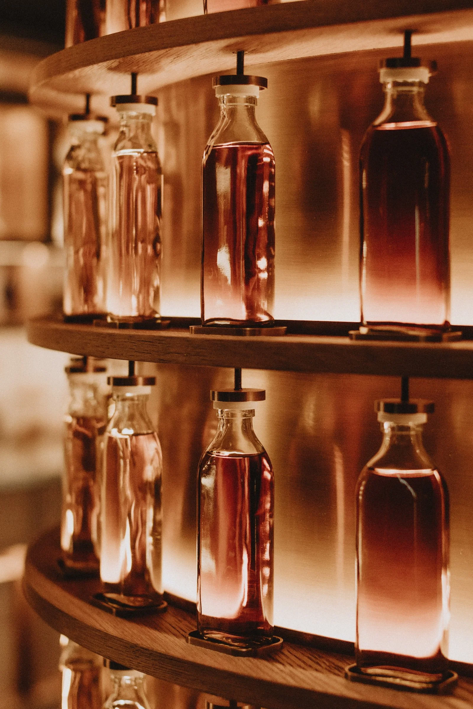 Glass bottles filled with pink liquid on wooden shelves, backlit for a warm glow.  Product Photography Chicago IL, Erin Drewitz Photography