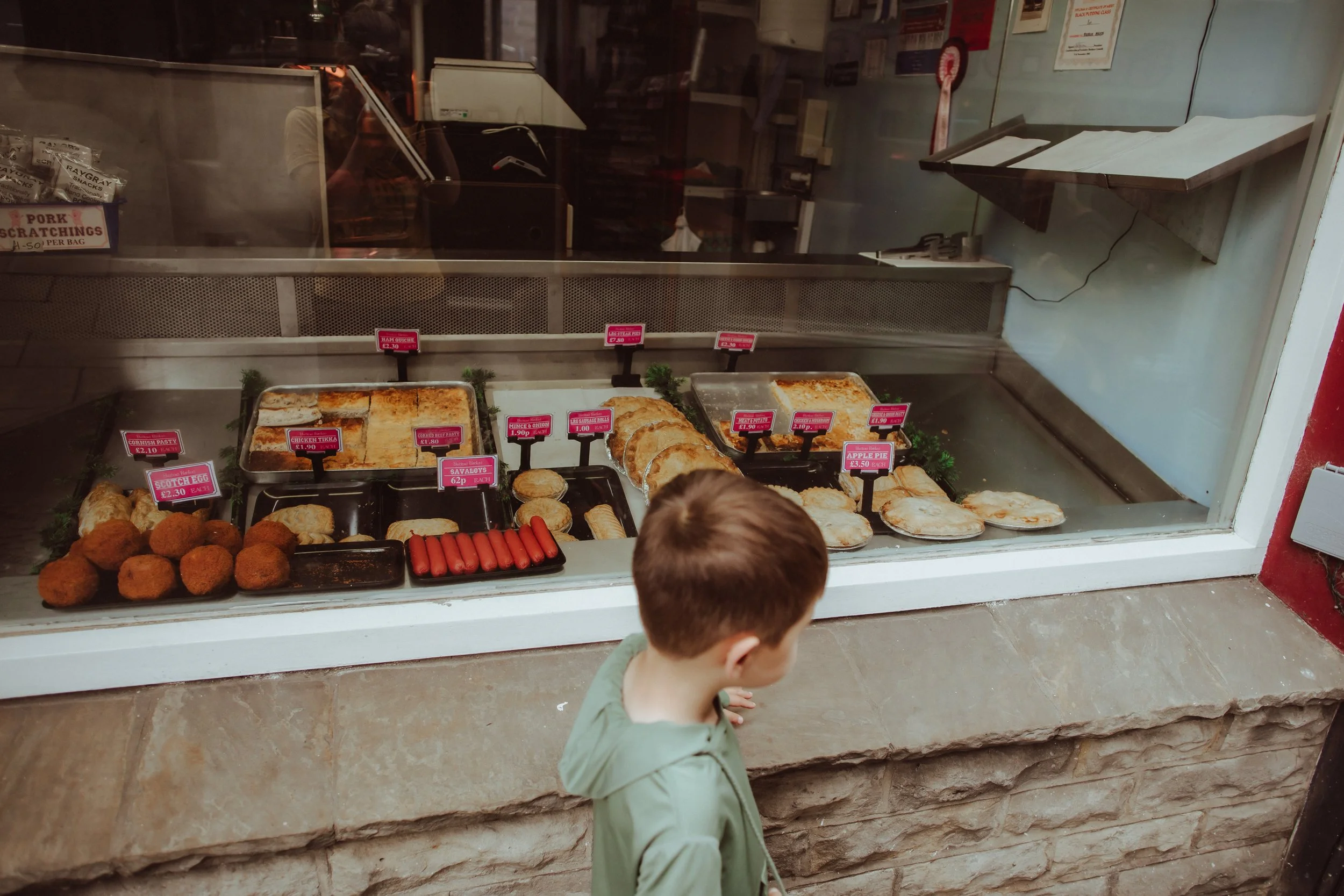 A young boy looking at a bakery display case filled with various baked goods and snack foods.