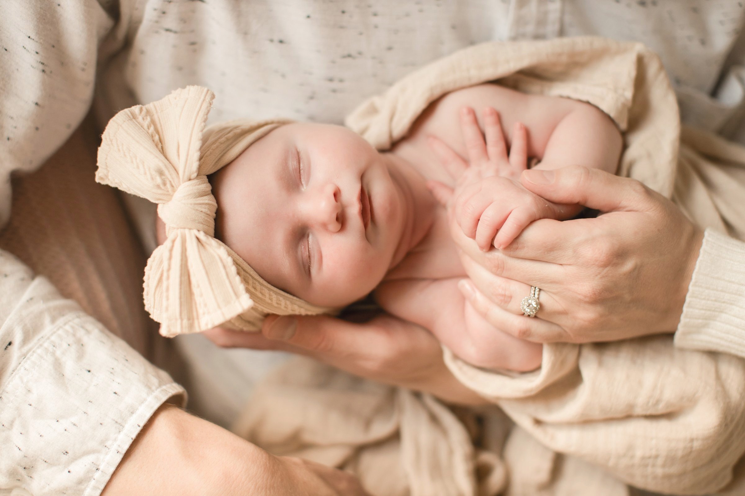 A sleeping baby with a headband and bow, gently held in an adult's hands.