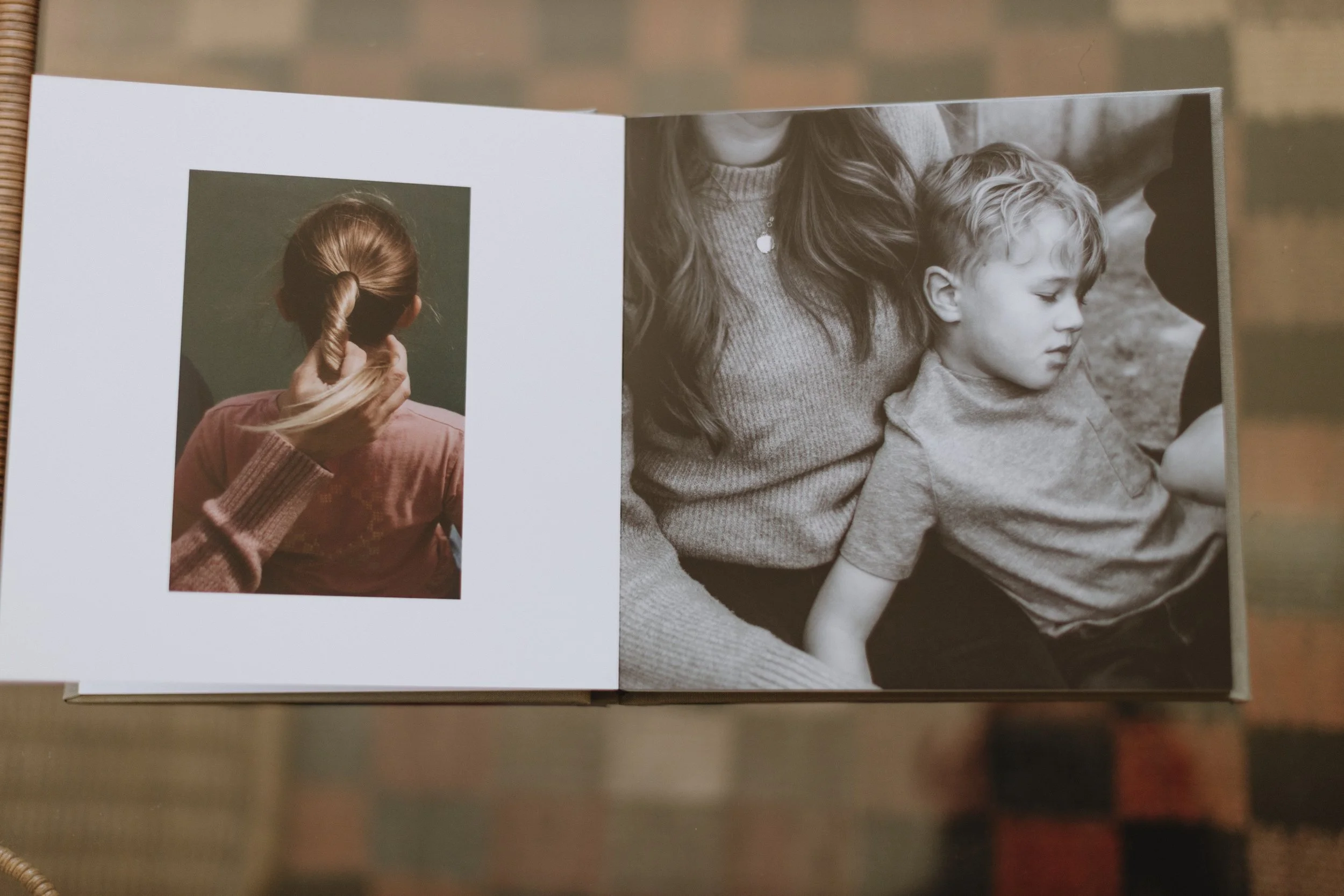 Open photo book showing a color photo of a woman with red hair in a ponytail holding a strand of her hair, alongside a black-and-white photo of a woman and a young boy with curly hair sitting close together.