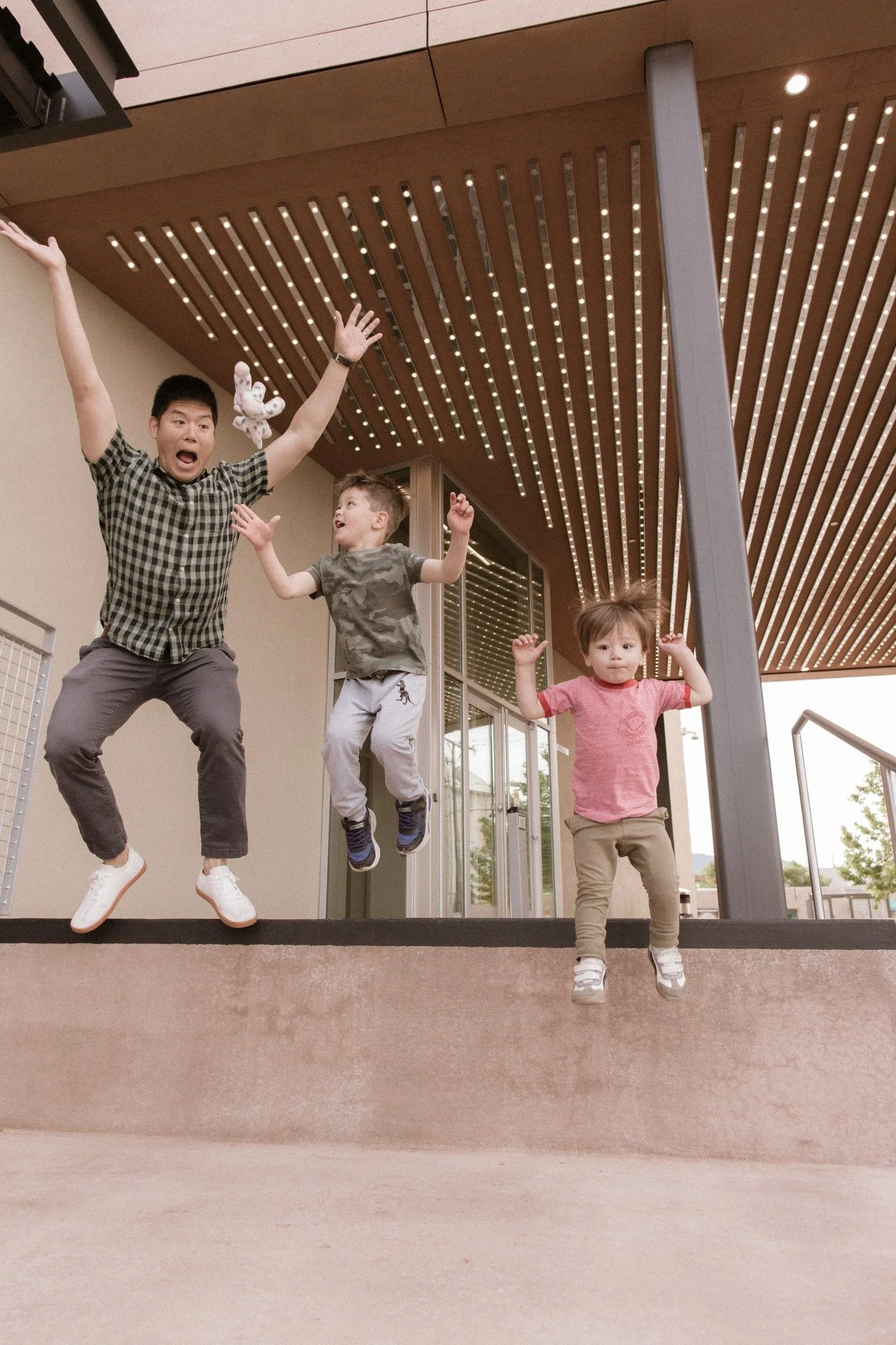 Three children and an adult jumping and playing on an indoor ledge, with a modern ceiling design featuring wooden panels and recessed lighting.