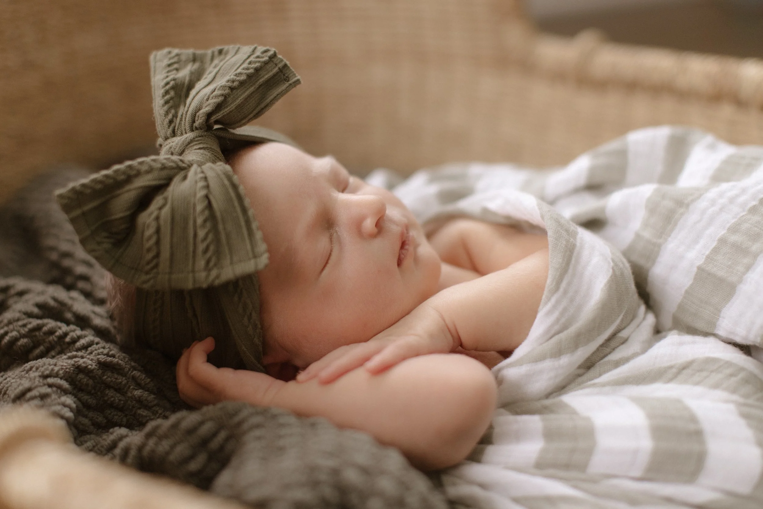 A sleeping baby girl with a large bow headband, wrapped in a striped blanket, resting on a textured brown surface.