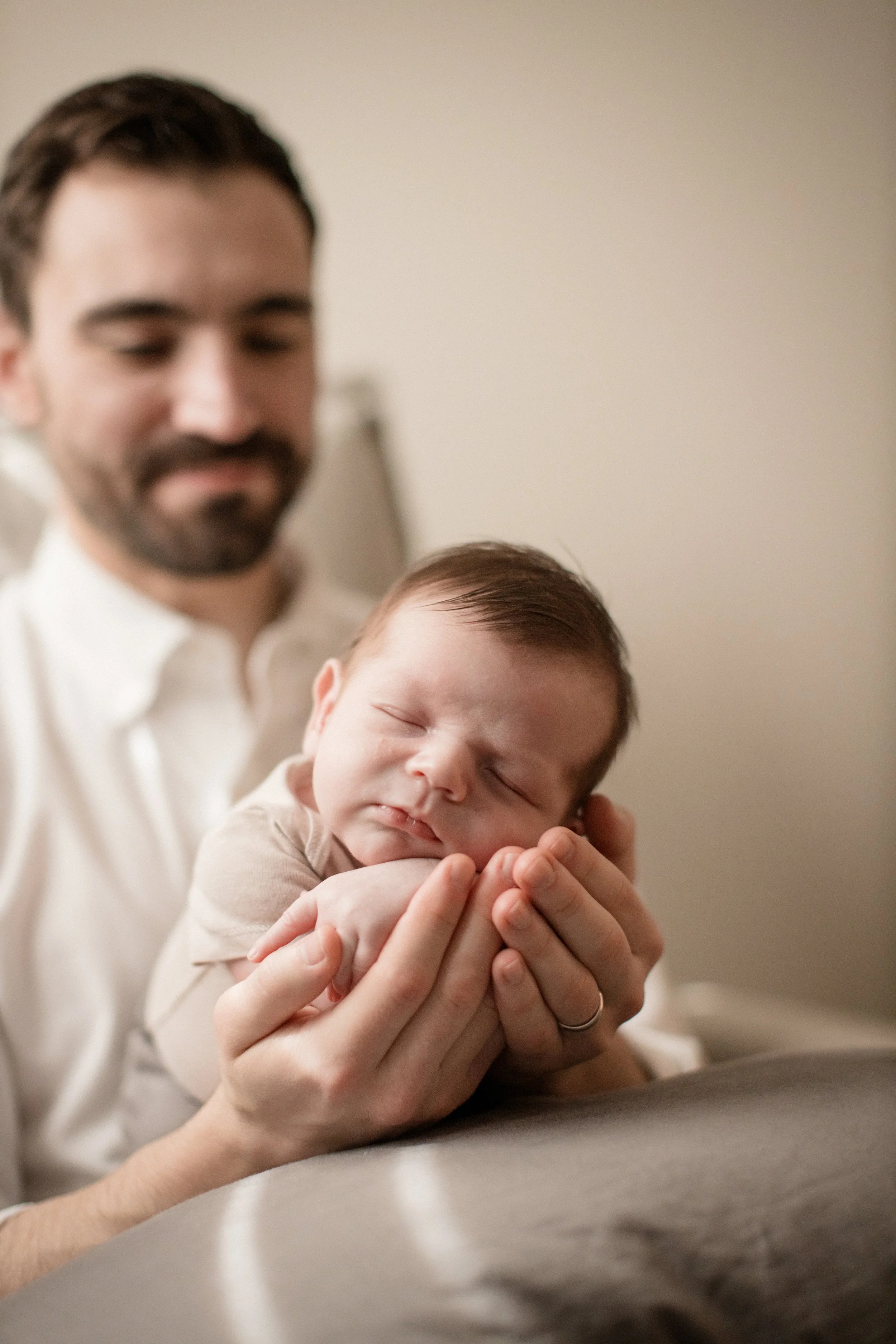 A man holding a sleeping baby in his hands, with the man slightly blurred in the background and the focus on the baby's peaceful face. Lifestyle newborn session shot in Evanston IL.