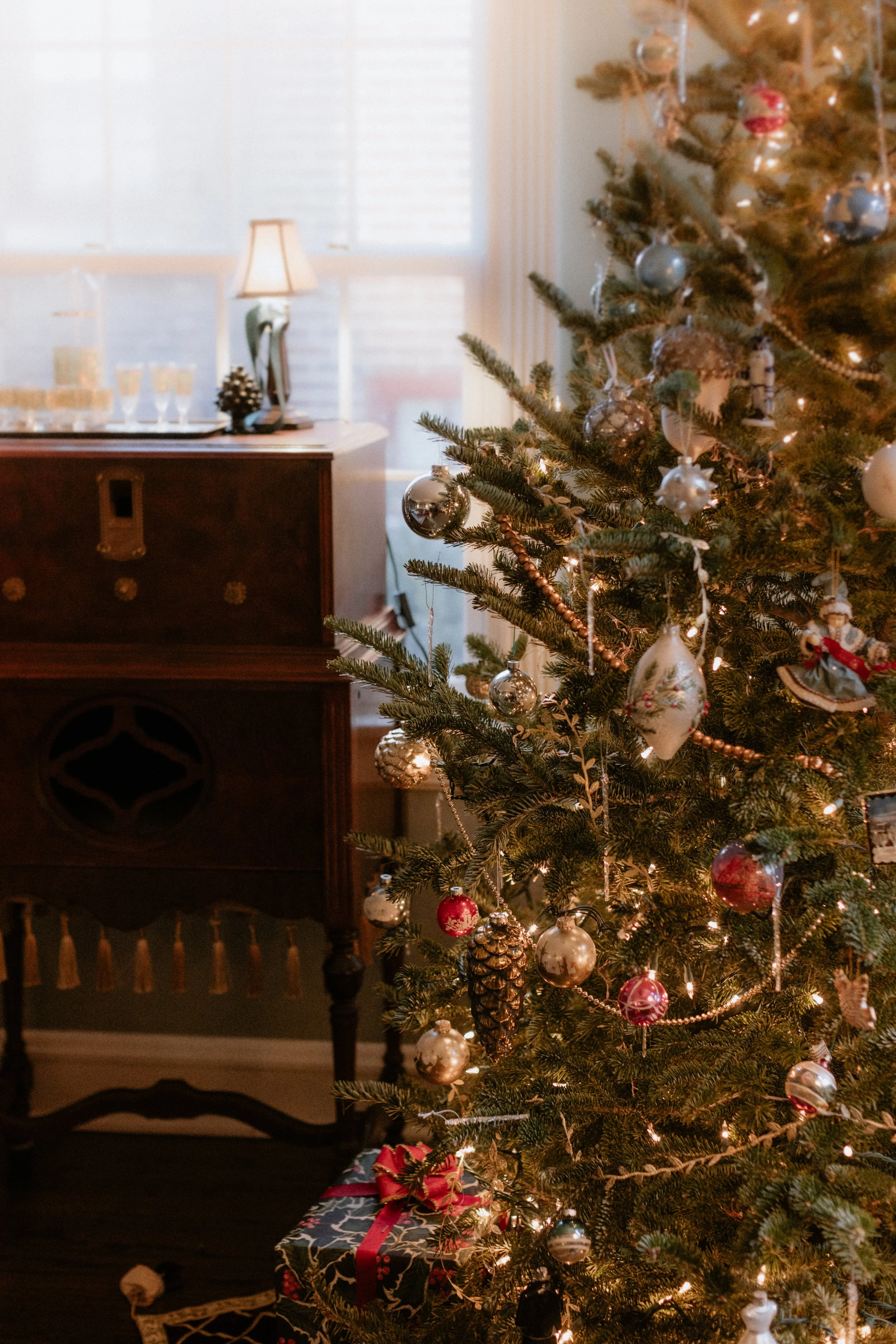 Decorated Christmas tree with ornaments and lights in front of a window, and a wrapped gift with a red ribbon underneath. Product Photography Shoot Evanston, IL.
