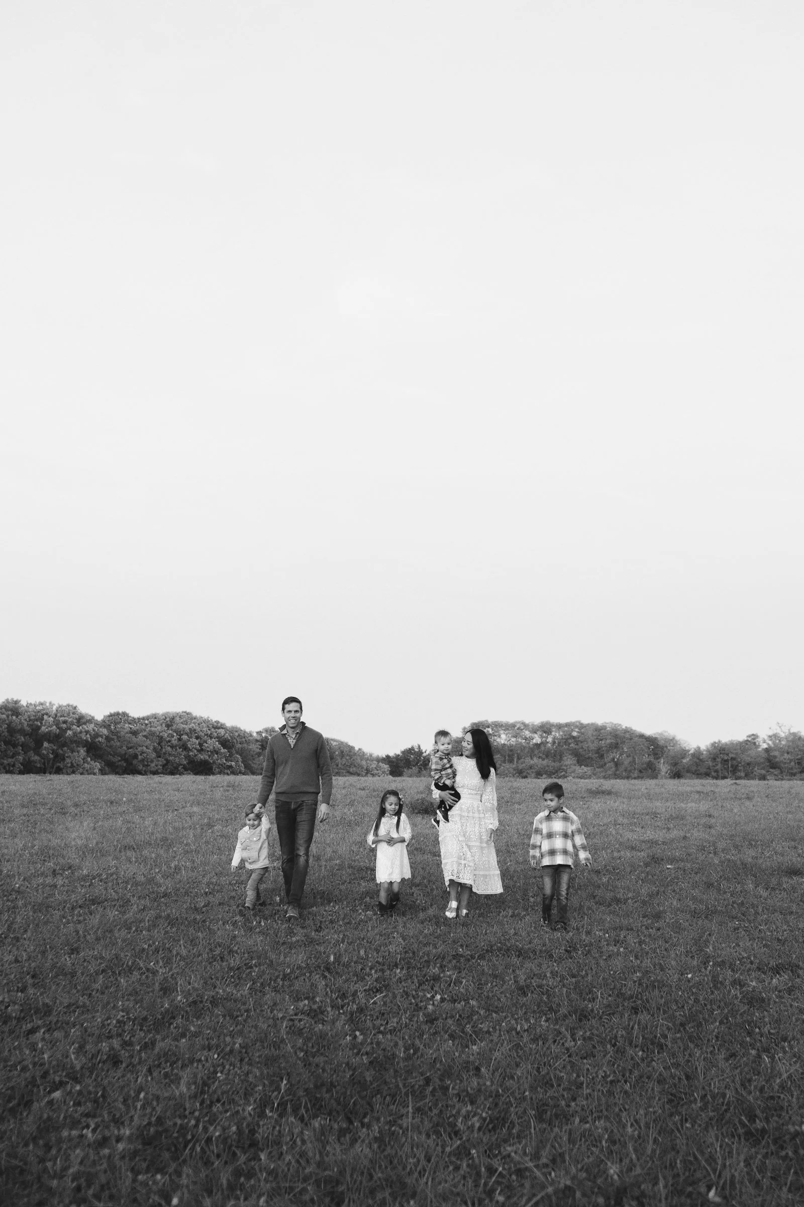 A family of six walking across an open grassy field, with trees in the background, in black and white.