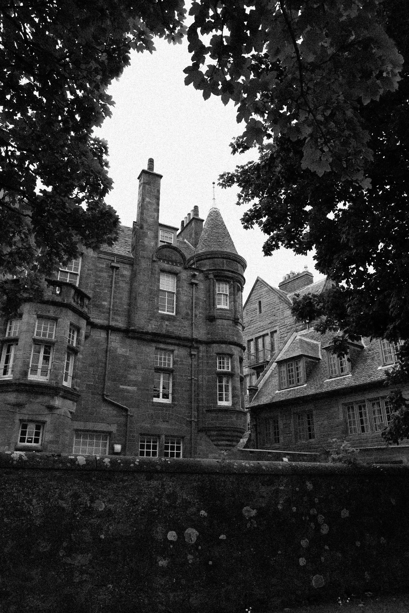 Black and white photo of a castle-like building with pointed towers, surrounded by trees.